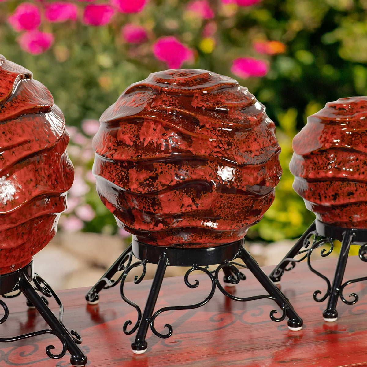A rounded red globe with glossy, uneven ridges sits between two partially visible globes on black stands.