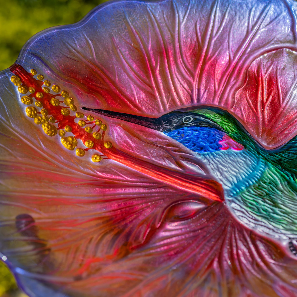 Close-up of the hummingbird’s head and golden flower details molded into the pink glass bowl.