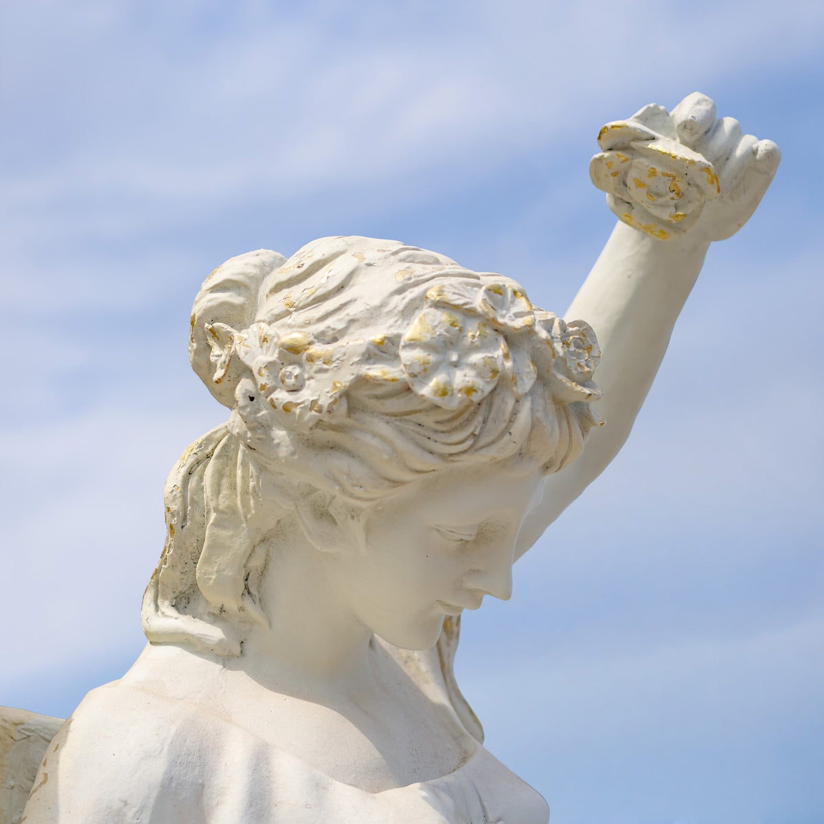 Close-up of the angel’s bowed face and curled hair, with one hand lifted against the sky.