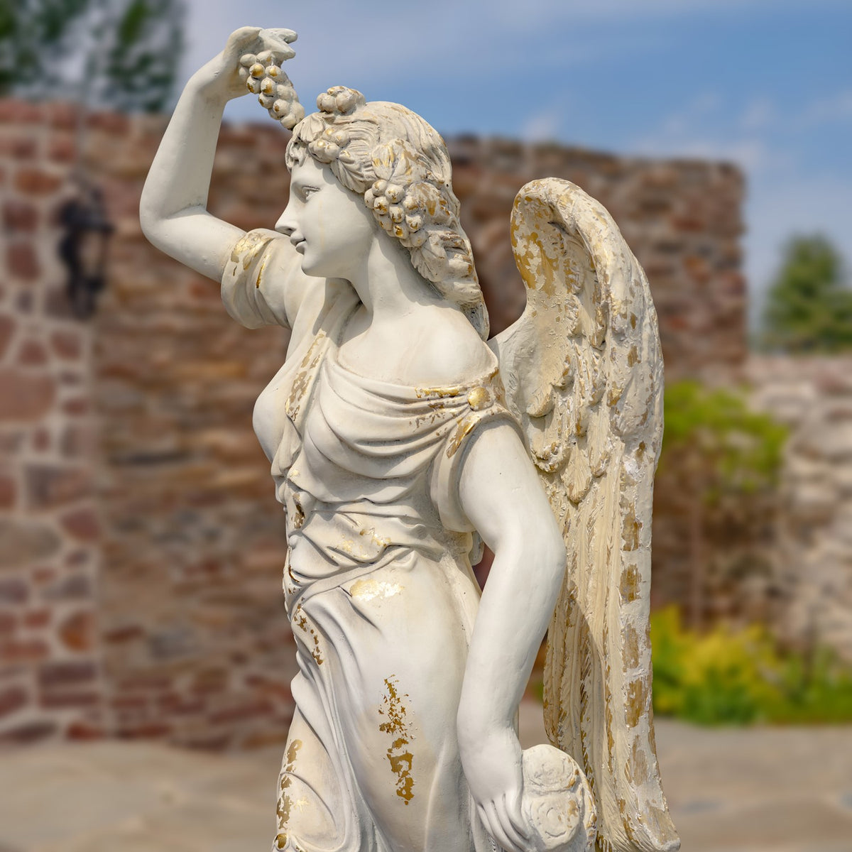 Angled view of the angel holding grapes overhead, with a weathered wing and gold-toned accents.