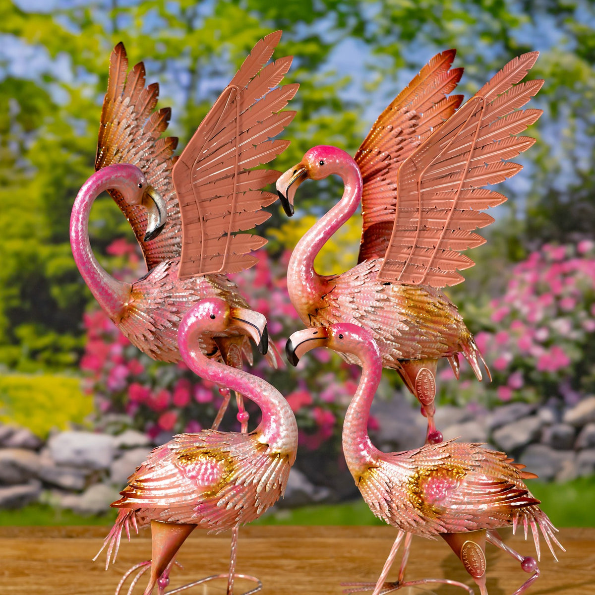 Four pink metal flamingo figurines with outstretched wings arranged together outdoors.