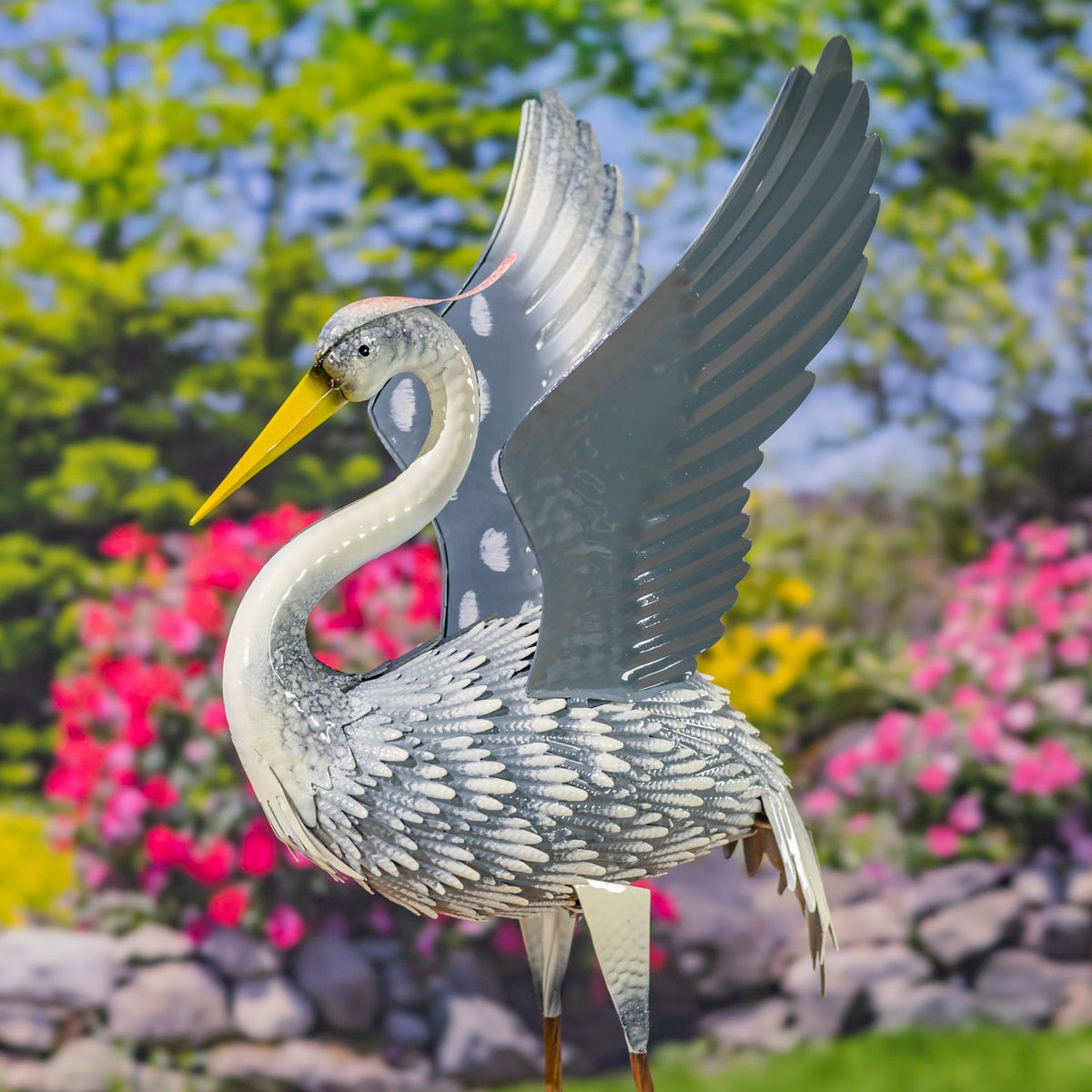 Close view of a metal heron with a curved neck, yellow beak, and tall raised wings.