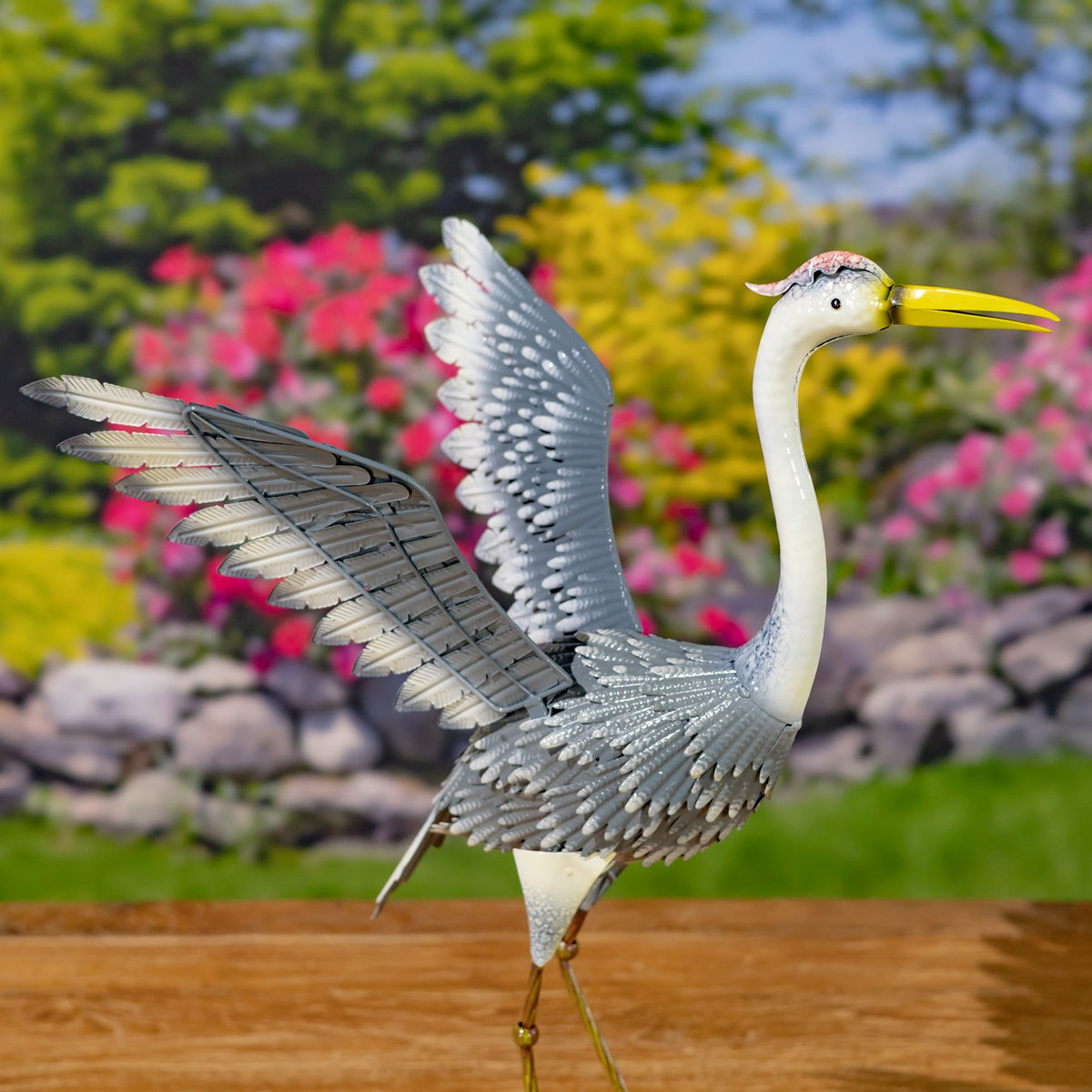 A gray-and-white metal heron stands with one wing raised and its long neck upright.