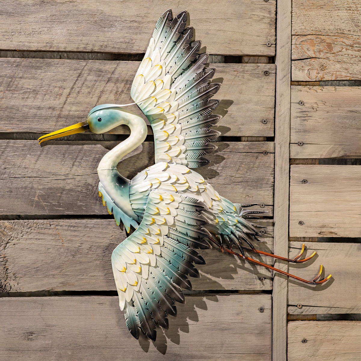 A crane wall decoration with raised wings and long legs, shown against rustic wooden planks.