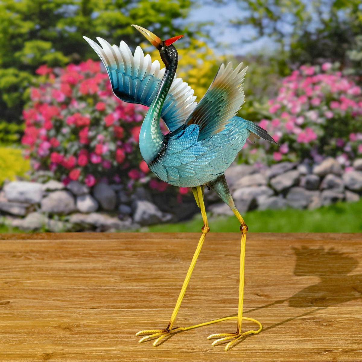 A blue heron figurine is shown from another angle, with its curved neck, layered wings, and yellow legs visible.