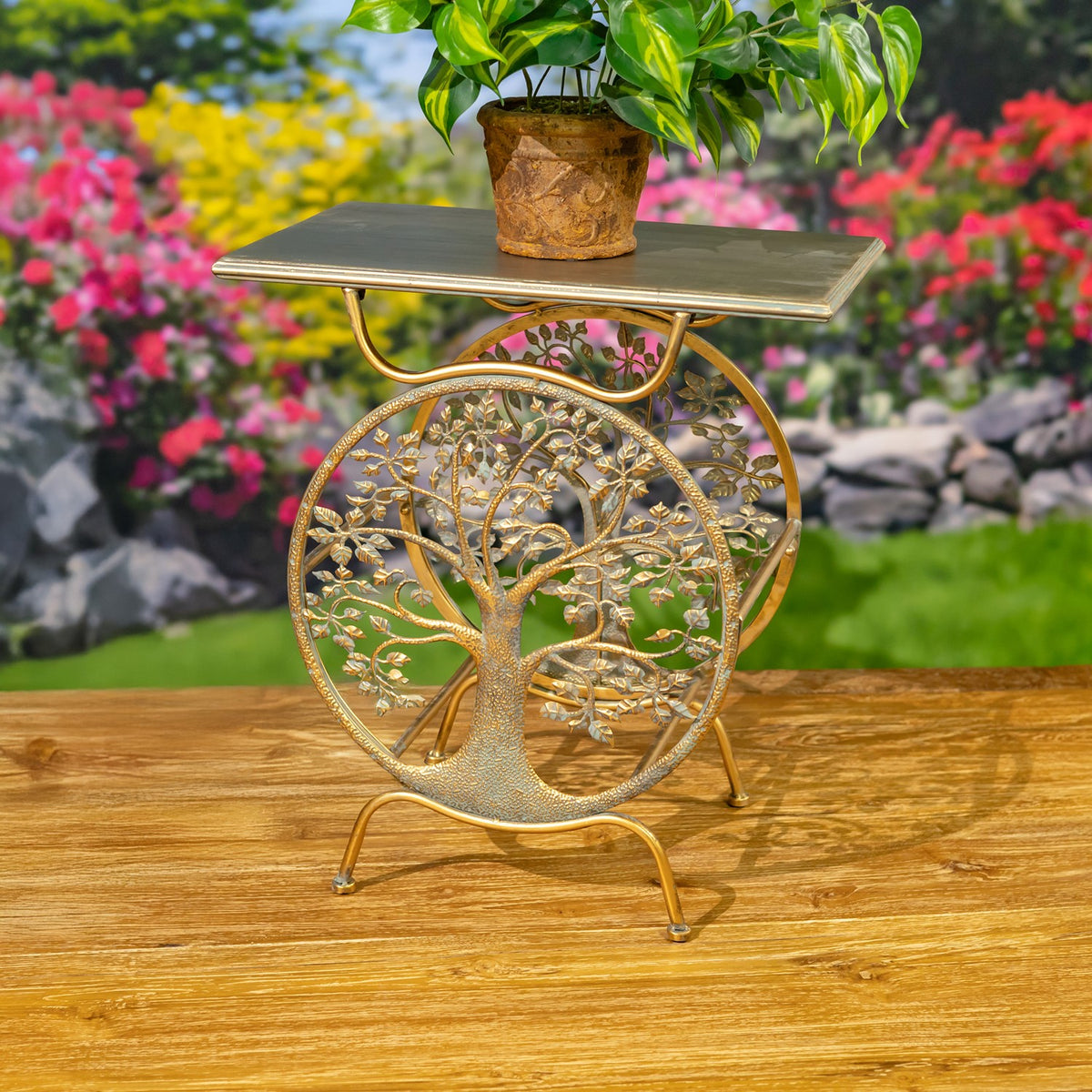 One gold tree-pattern plant stand and potted greenery on a wooden deck, viewed from the side.