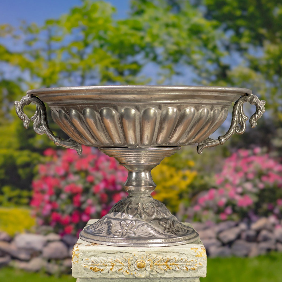 Close view of a silver urn’s fluted bowl, curled handles and patterned pedestal base.