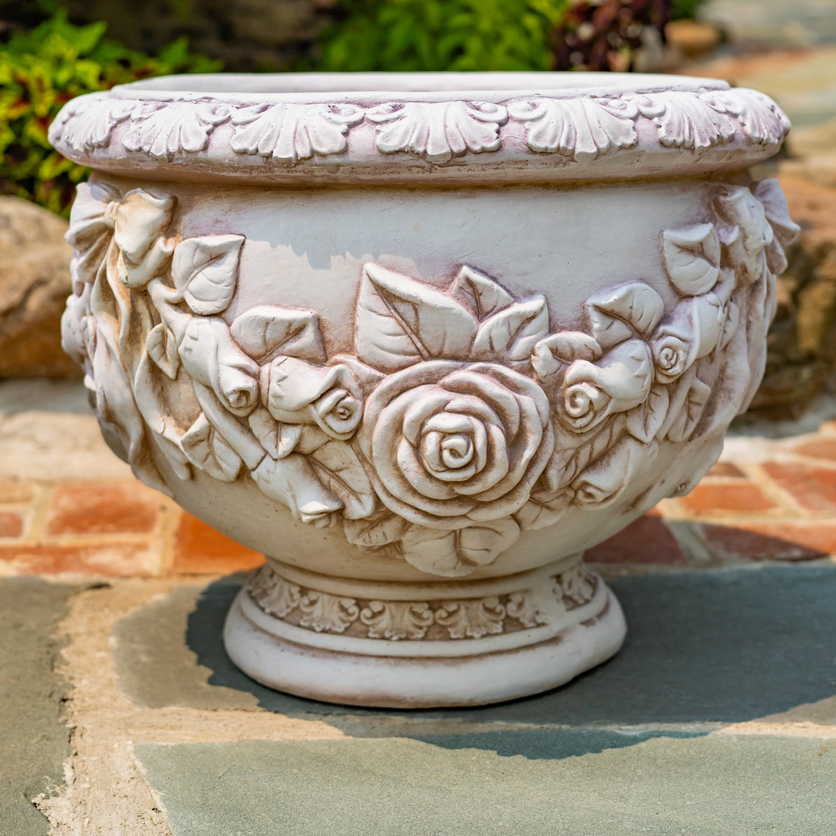 Close view of a pale urn planter with raised roses, leaves, and an embellished rim.