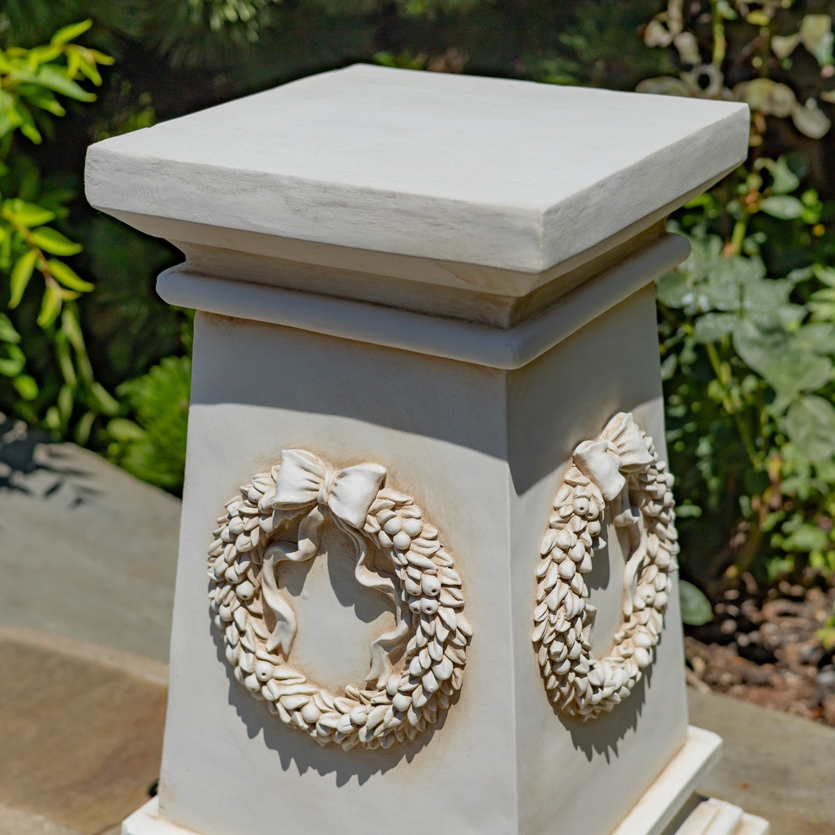 Close view of the column's square top and sculpted wreath ornament against its light-colored surface.