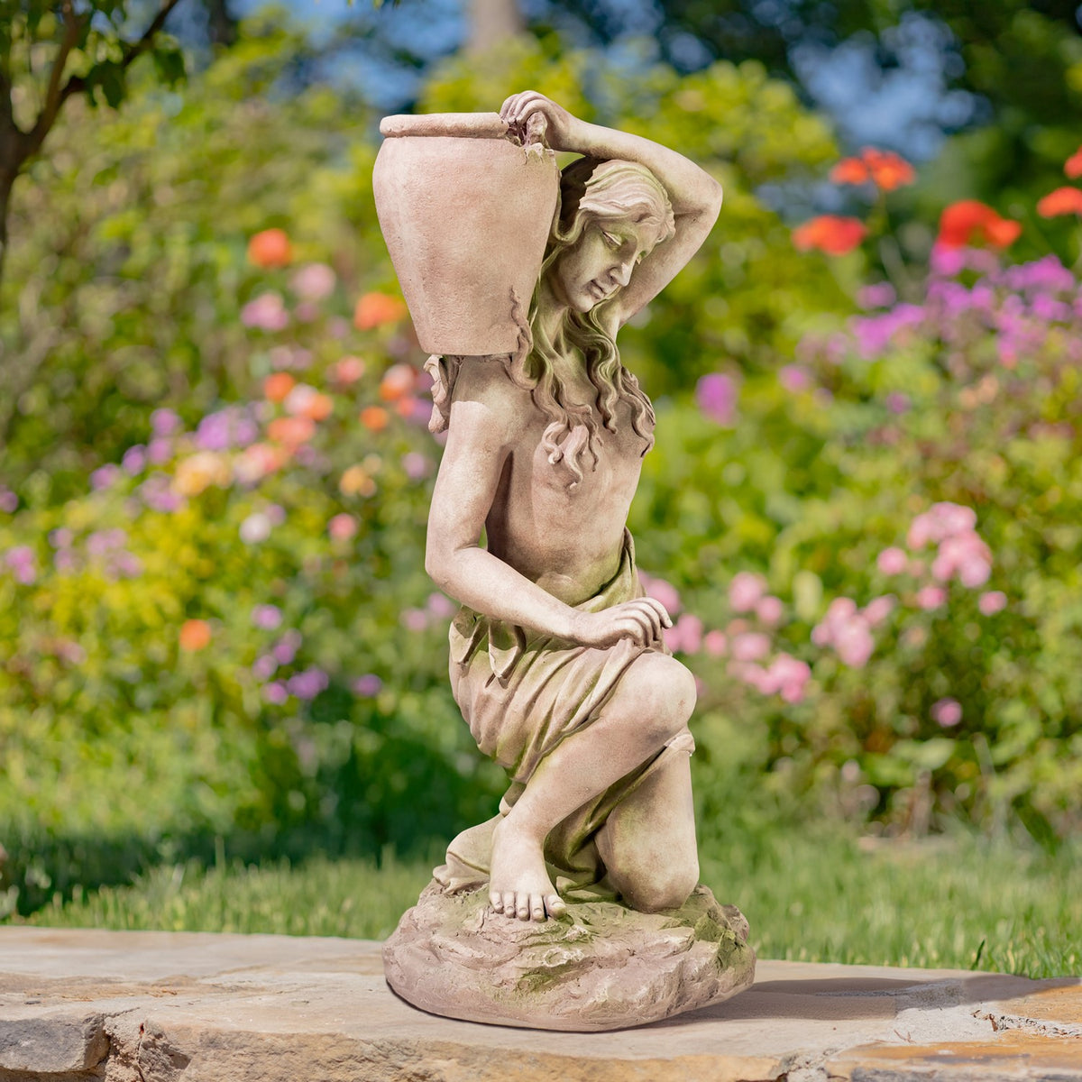 Full view of a kneeling woman statue with an urn, shown on a stone base outdoors.