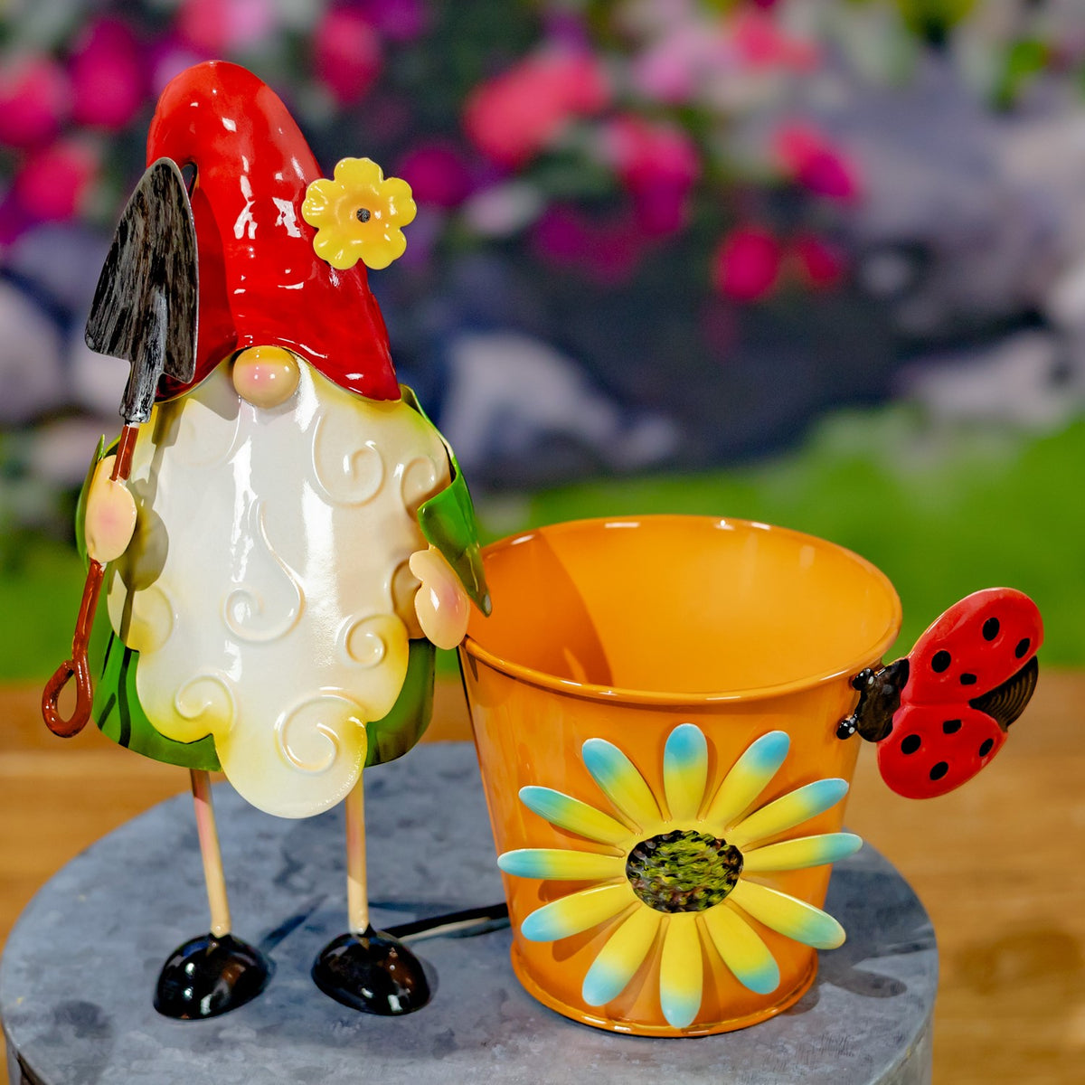 An orange flower pot with a painted daisy and ladybug sits beside a gnome in a red hat.