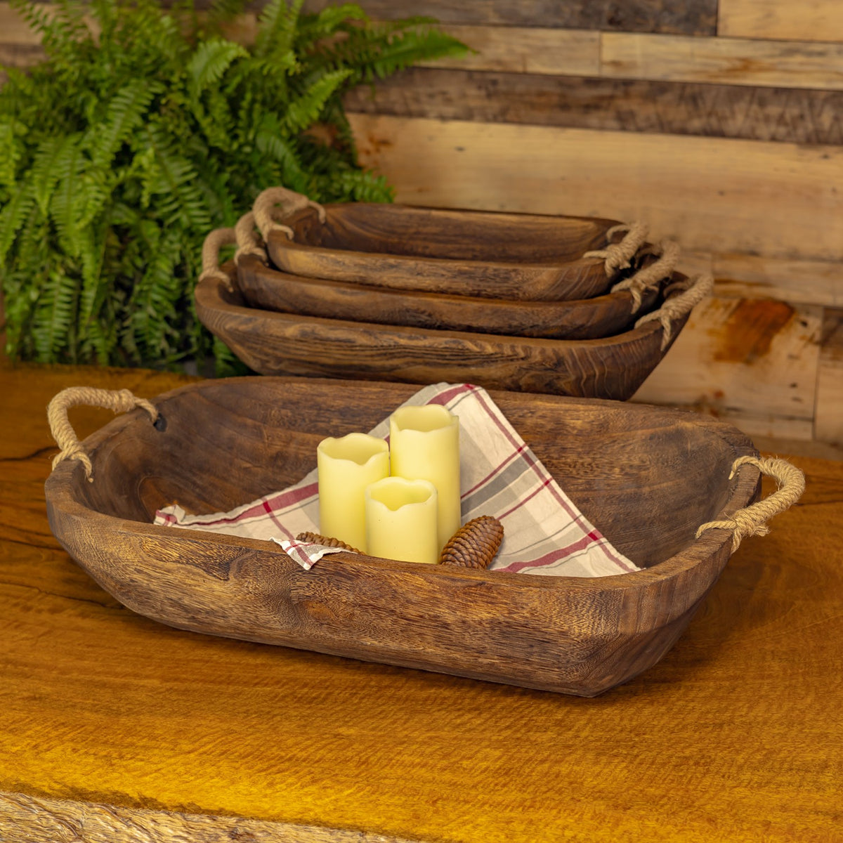 A wooden tray holding candles and folded cloth sits in front of three nested trays.