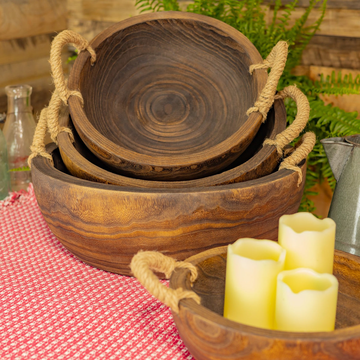 Nested wooden trays show their dark circular grain and rope handles, beside a tray holding candles.