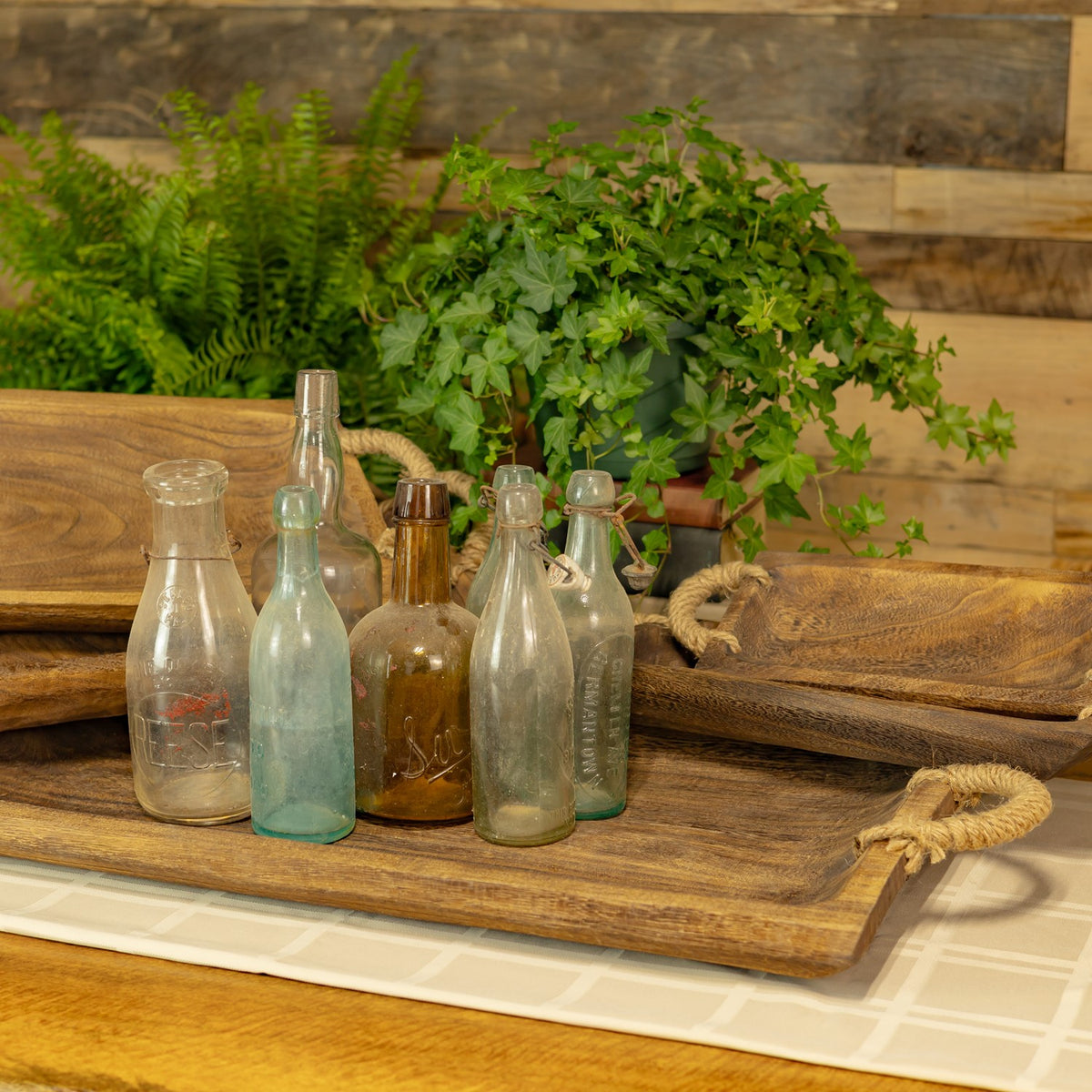 Brown wooden trays with rope handles beside glass bottles and greenery