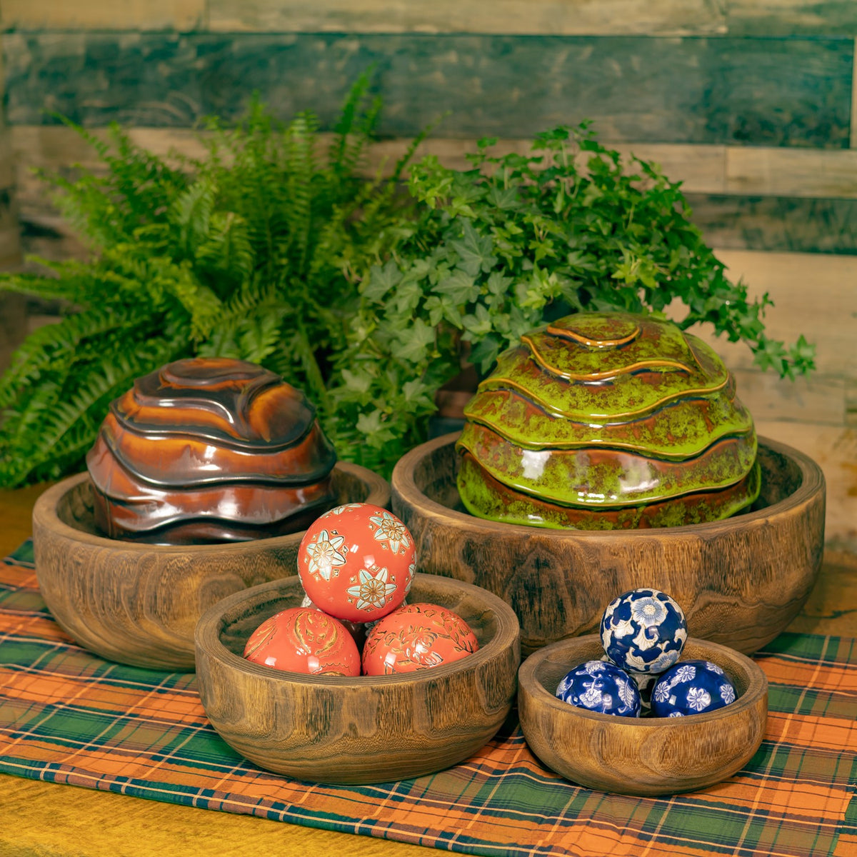 Four wooden bowls displayed with colorful decorative objects inside against a leafy backdrop.