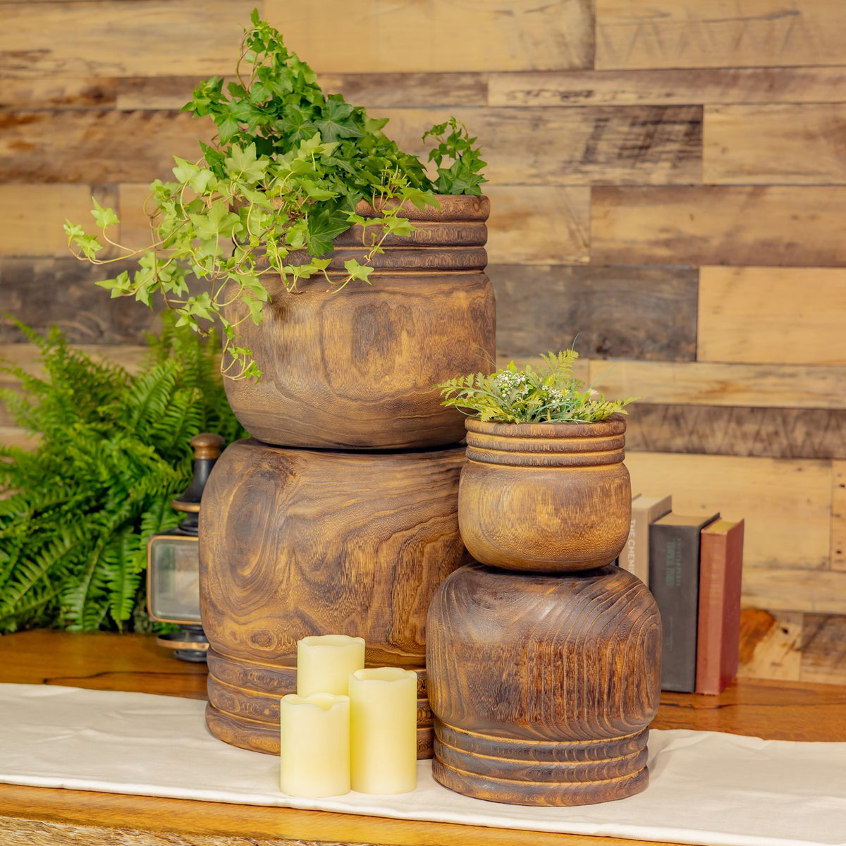 Four wooden bowls stacked at different heights with greenery and cream candles in front.