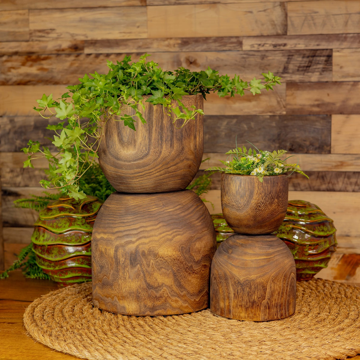 Four wooden bowls stacked in pairs, with greenery and small flowers in two bowls.