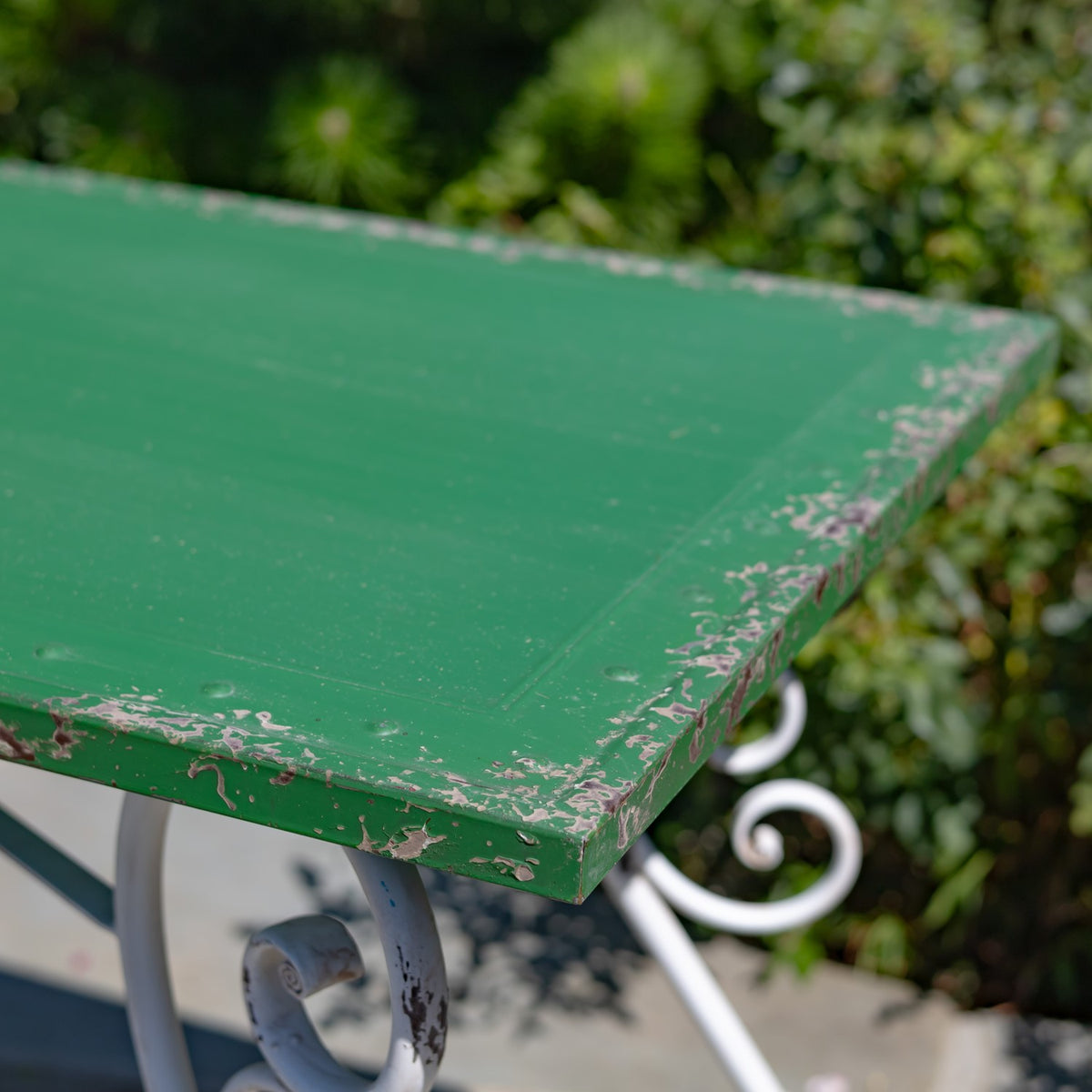 Close-up of the worn green tabletop edge, with chipped paint and part of a curled metal support visible.