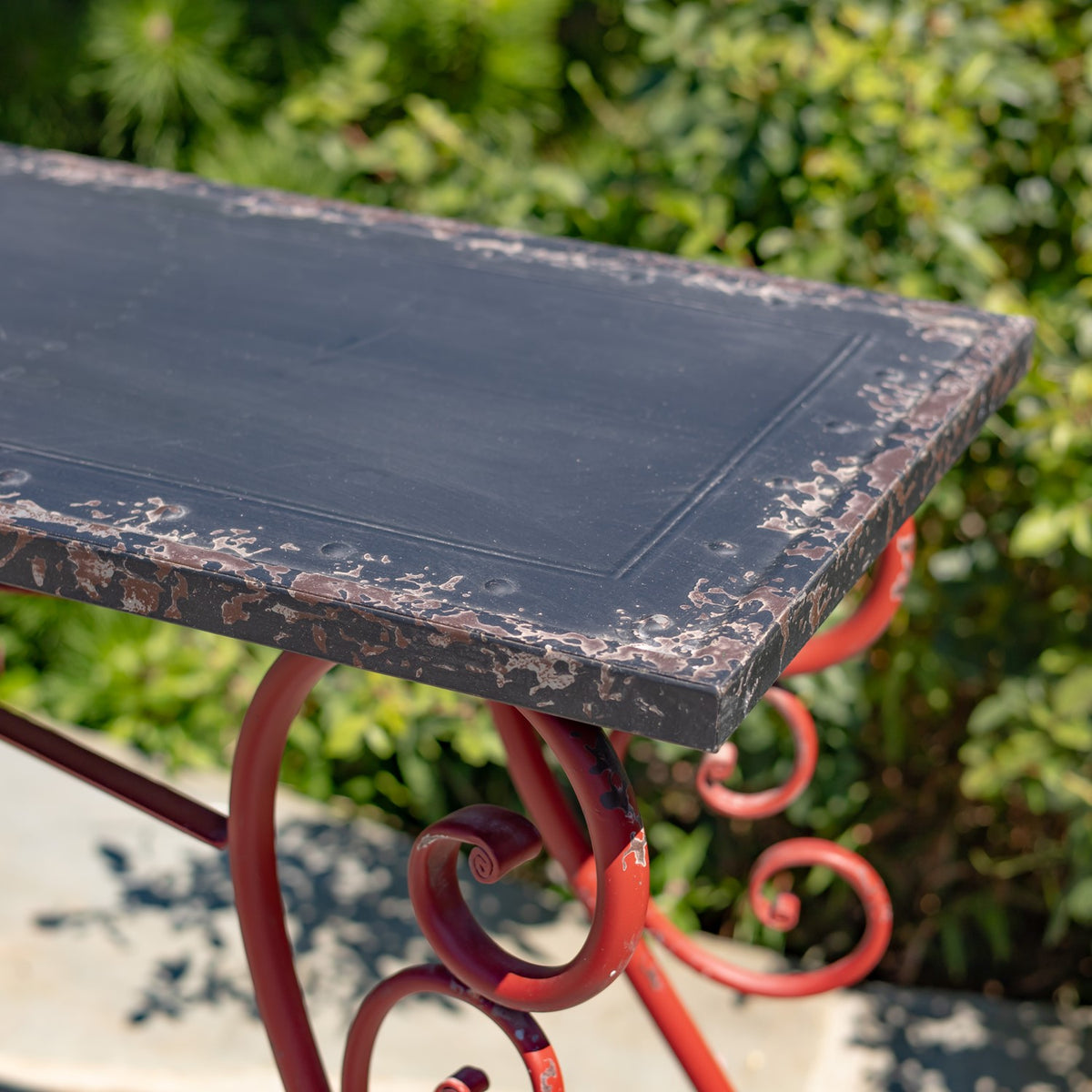 Close-up of a dark tabletop with worn, chipped edges above a red curled metal support.