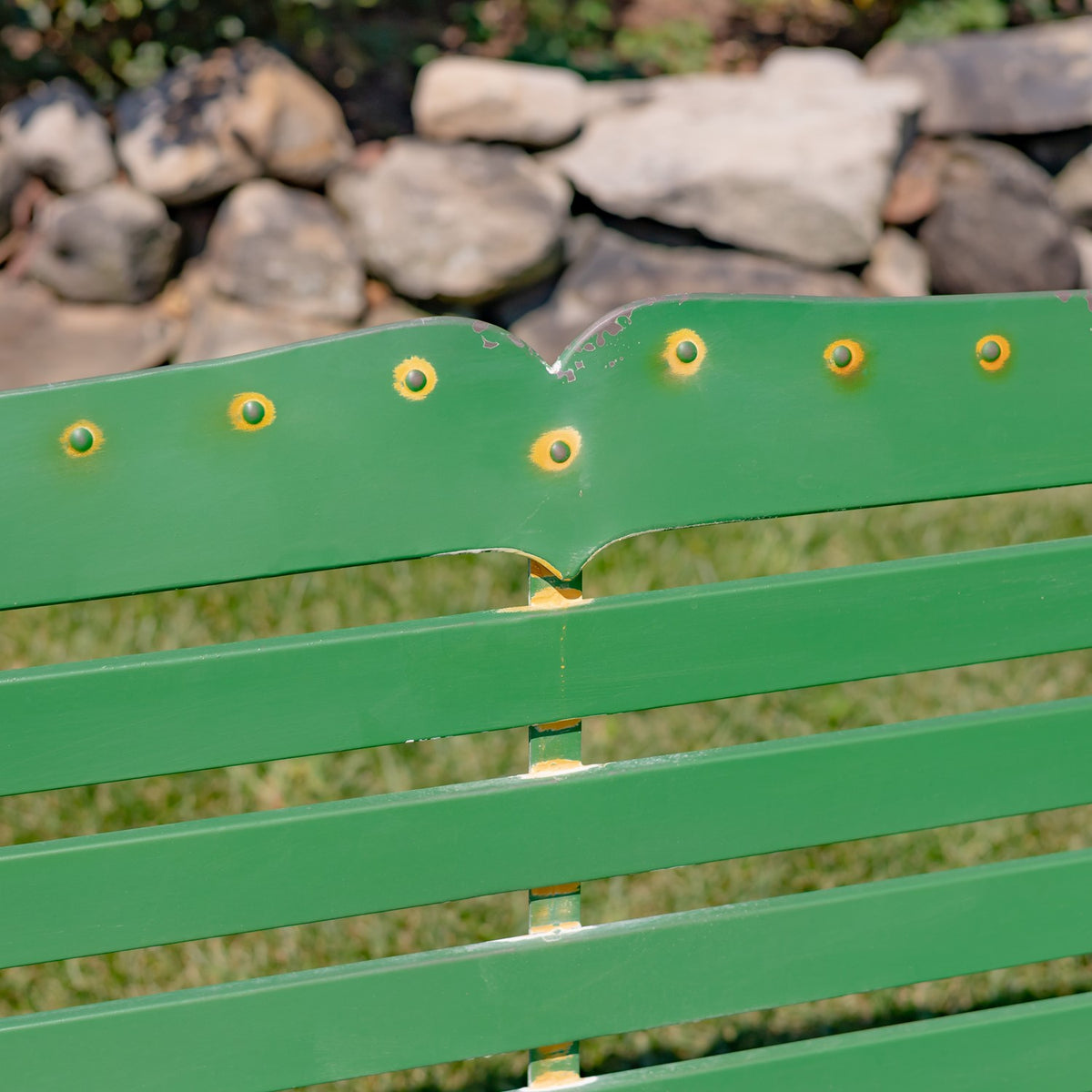 Close-up of the bench’s green backrest, showing gold-toned round accents and worn paint along the edges.