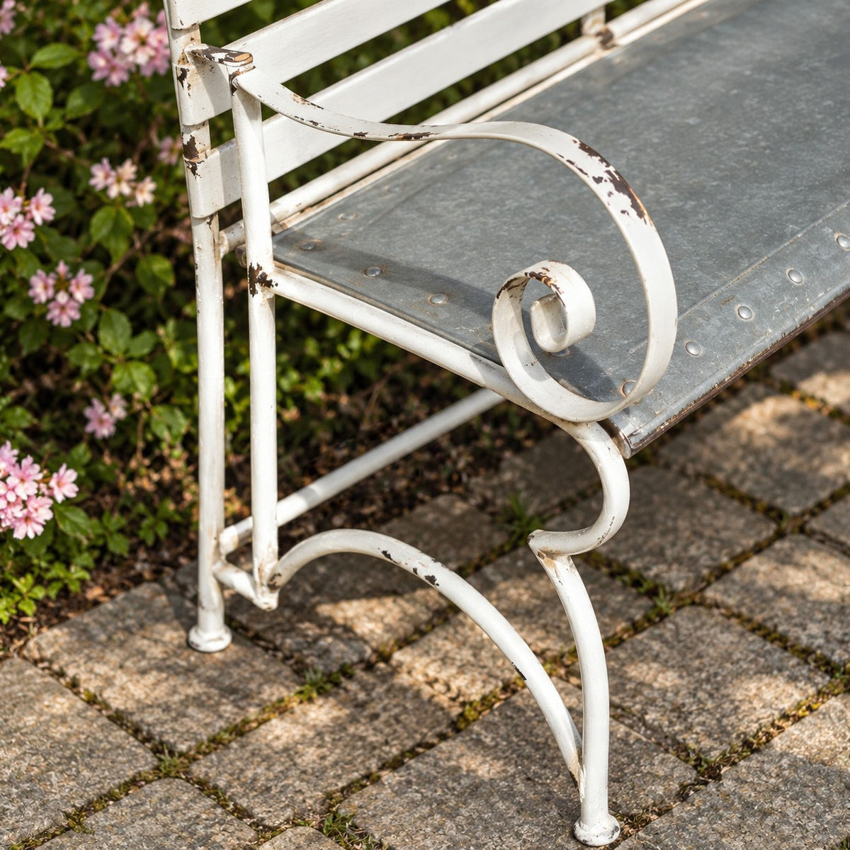 Close-up shows the bench’s curled white arm, curved leg, dark seat, and chipped paint.