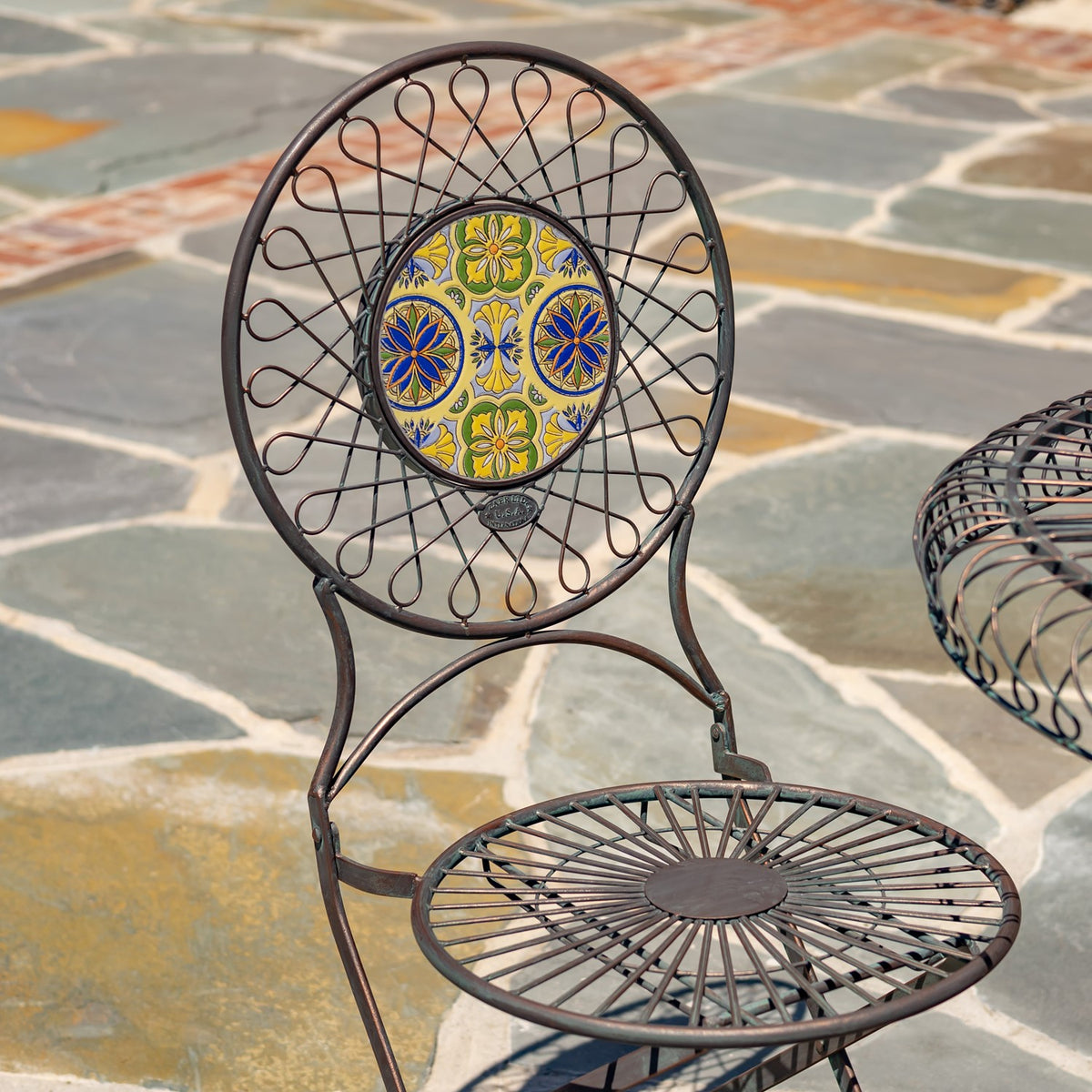 A wire-frame chair with a circular yellow-and-blue mosaic back and radial wire seat.