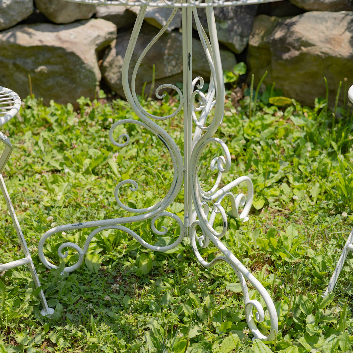 Close-up of the table’s curled wire pedestal and feet against the garden ground.