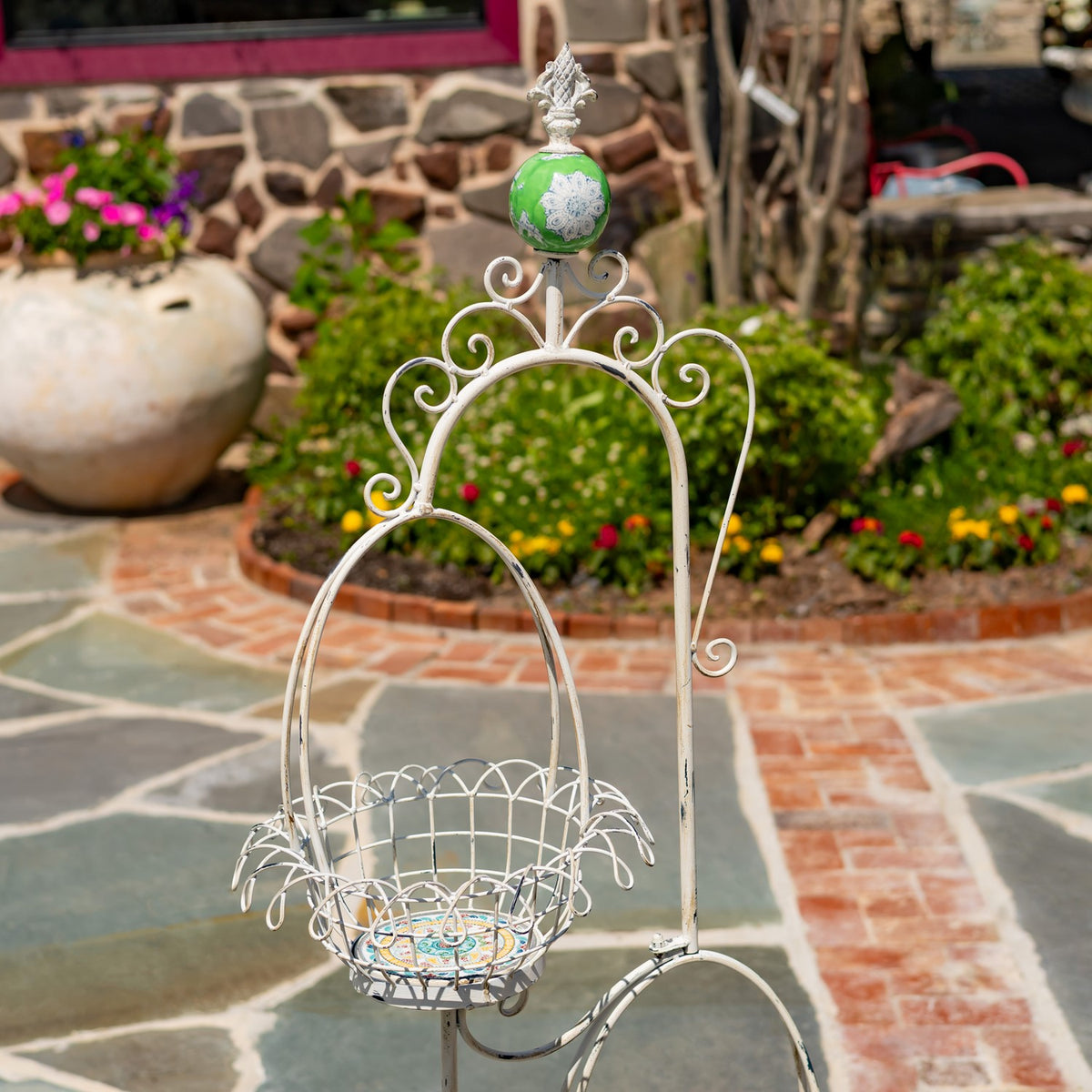 Close view of the upper wire basket, curved frame, and green ornament atop the plant stand.