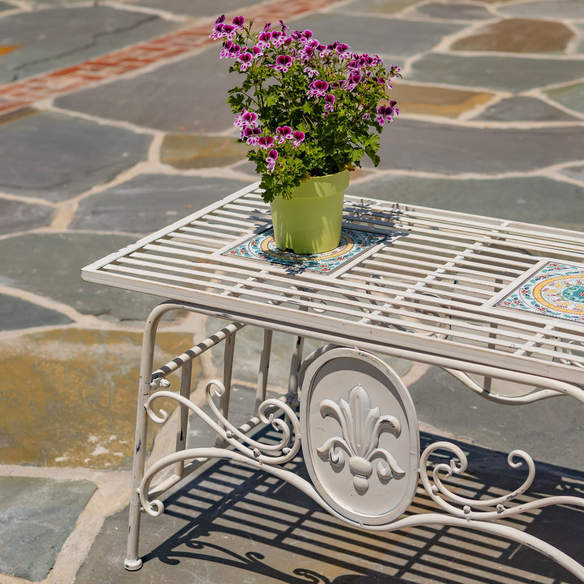 Closer view of the slatted tabletop, colorful mosaic inset, and a potted flowering plant.