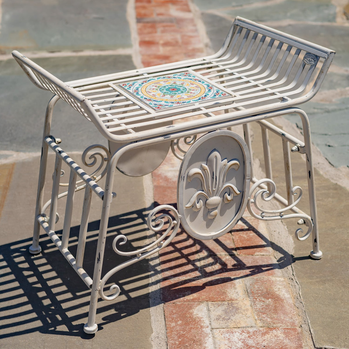 Angled view of the chair's raised ends, patterned mosaic panel, and curled metal supports on stone paving.