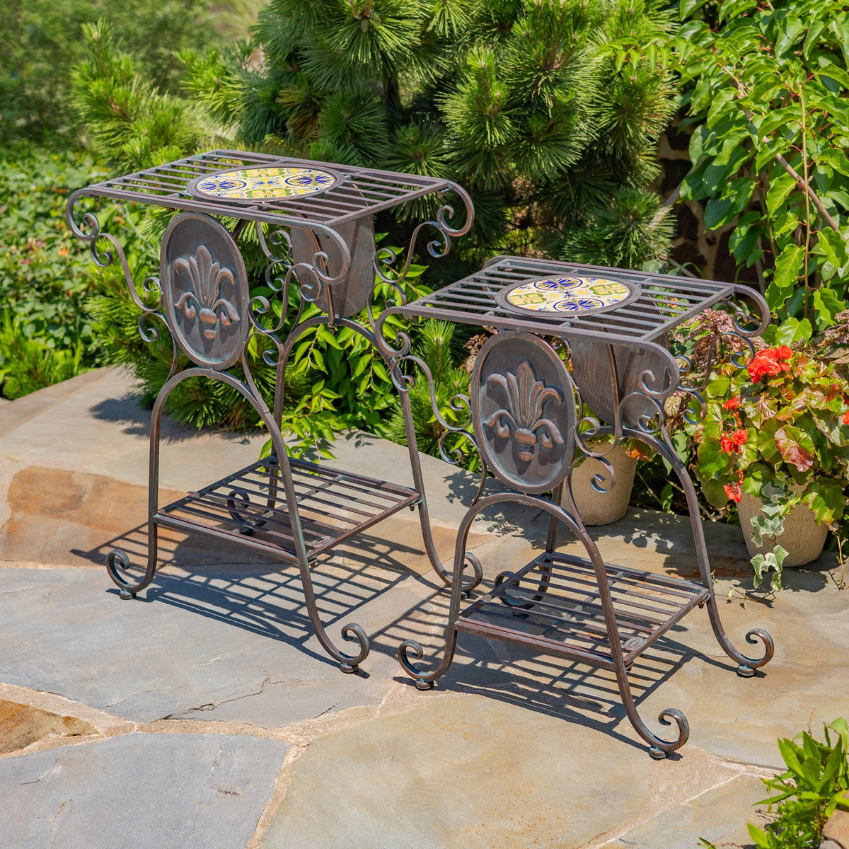 Two scrollwork plant stands with patterned mosaic tile centers on a sunlit patio.