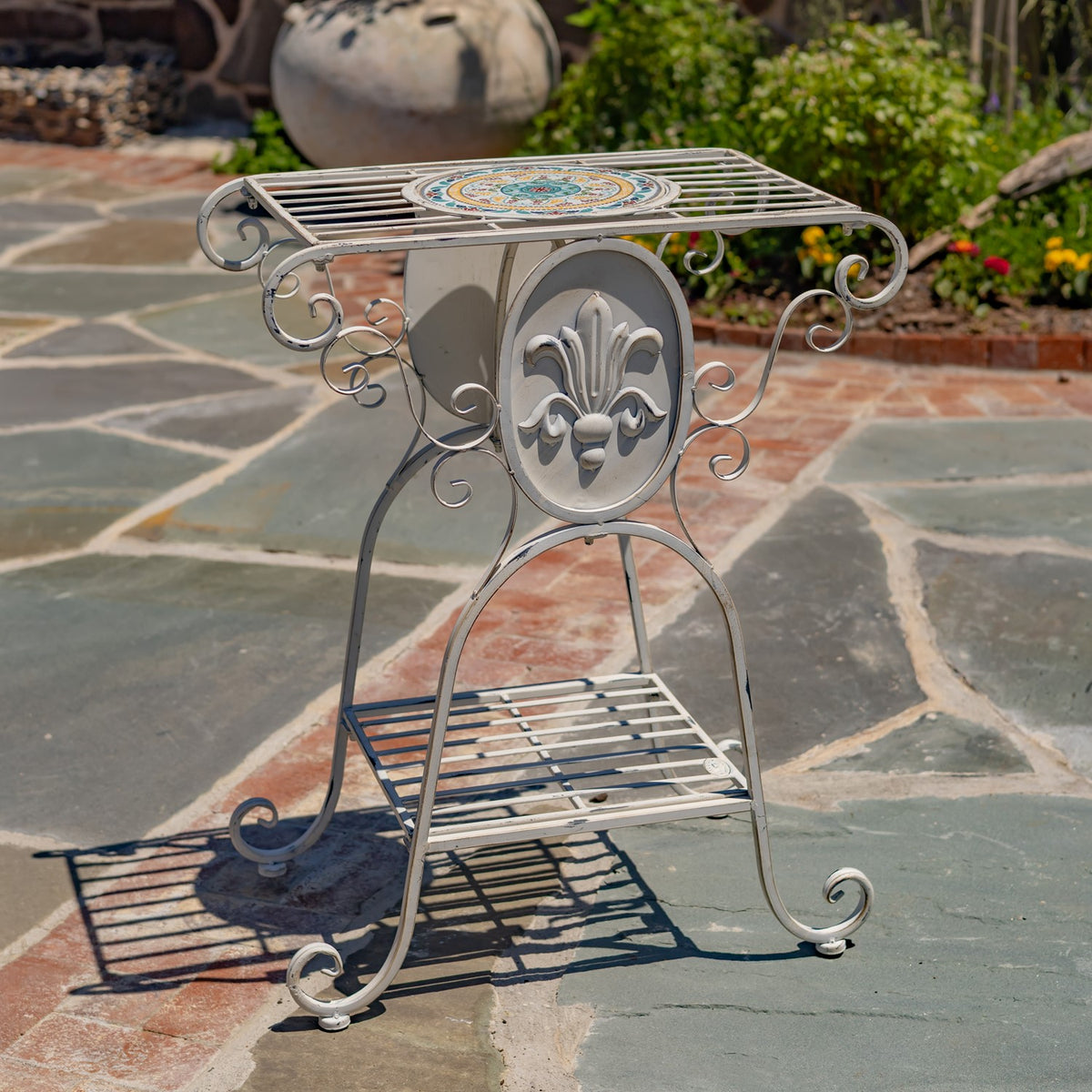 One metal plant stand with curled legs, a fleur-de-lis panel, and a colorful mosaic top.