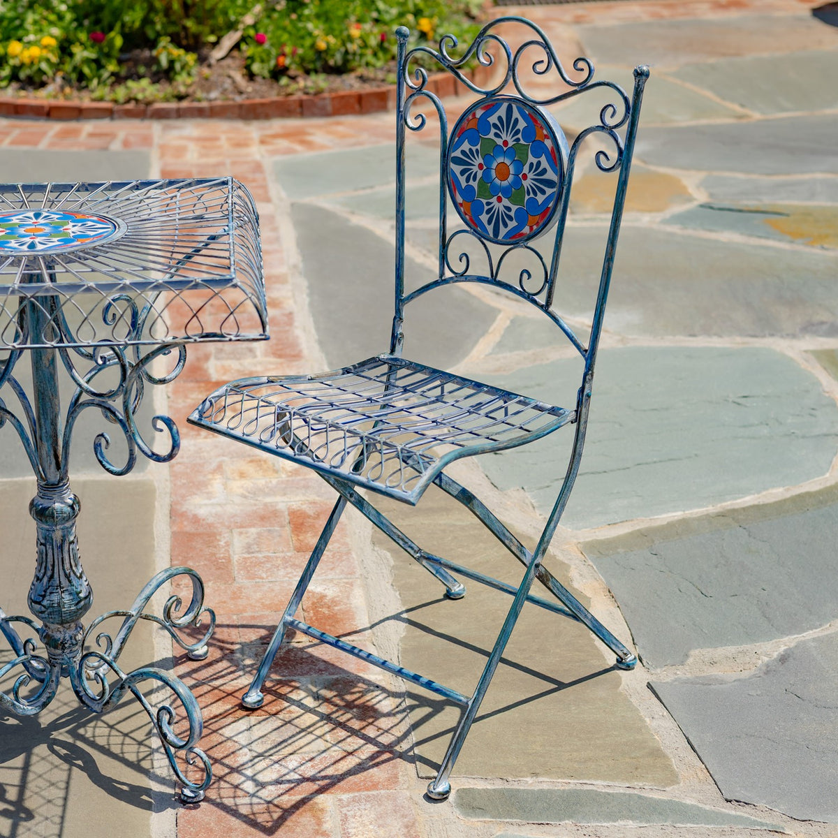 A matching bistro chair with a colorful circular mosaic in its scrollwork back, beside the table.