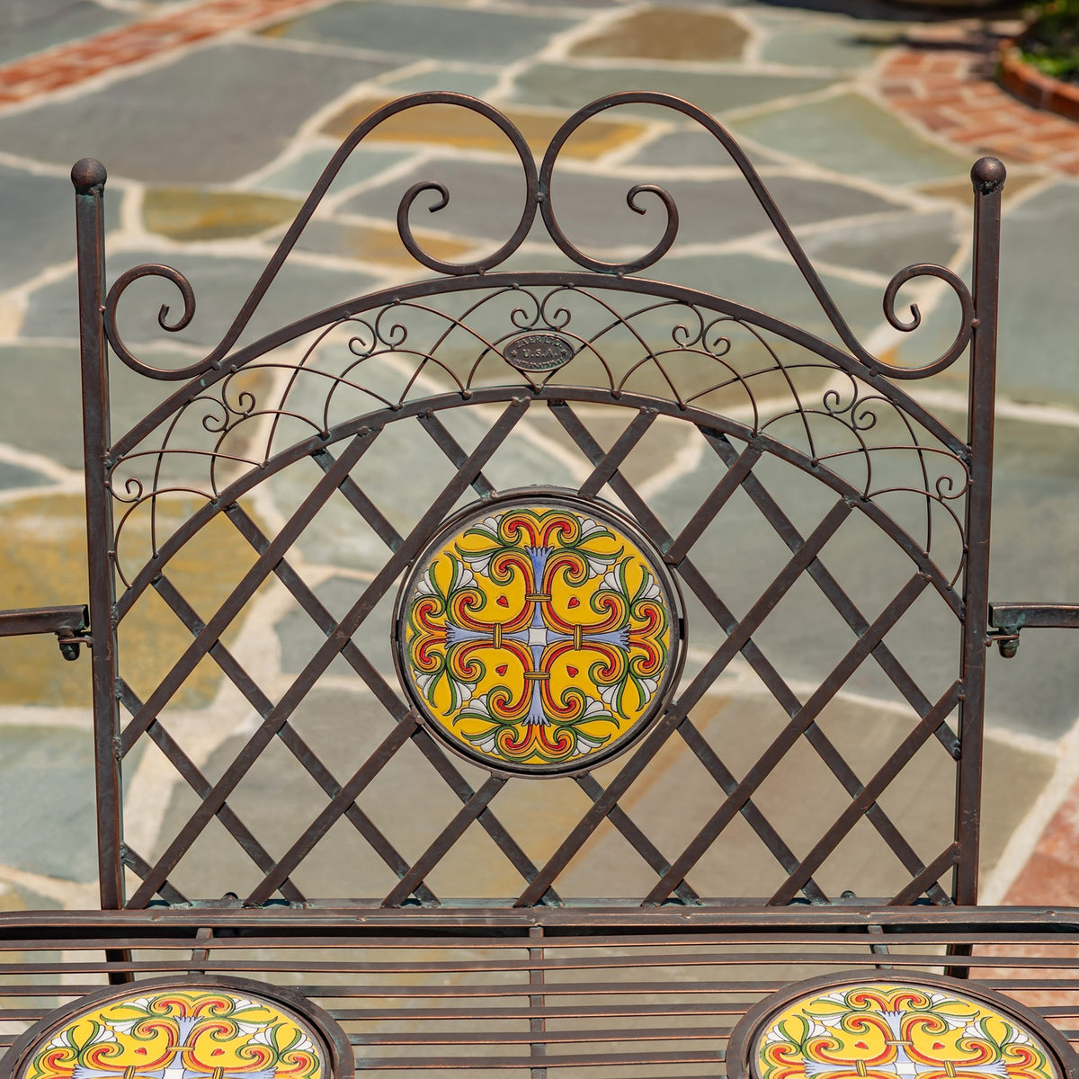 Close view of the bench's scrollwork backrest and round yellow, orange, and red mosaic centerpiece.