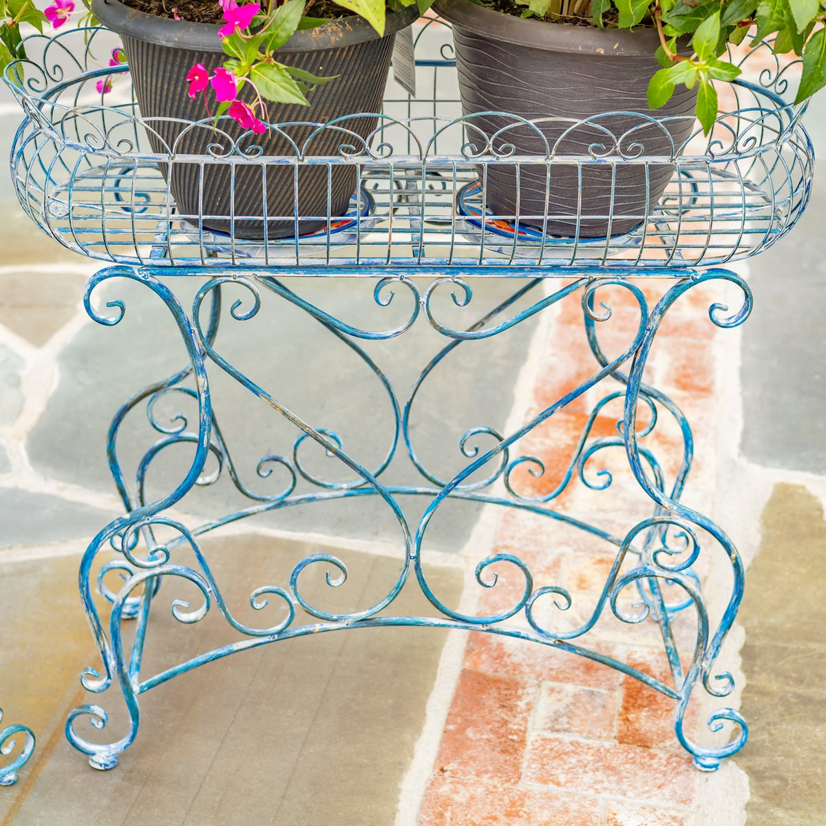 Close view of an oval basket stand with potted plants and decorative scrollwork legs.