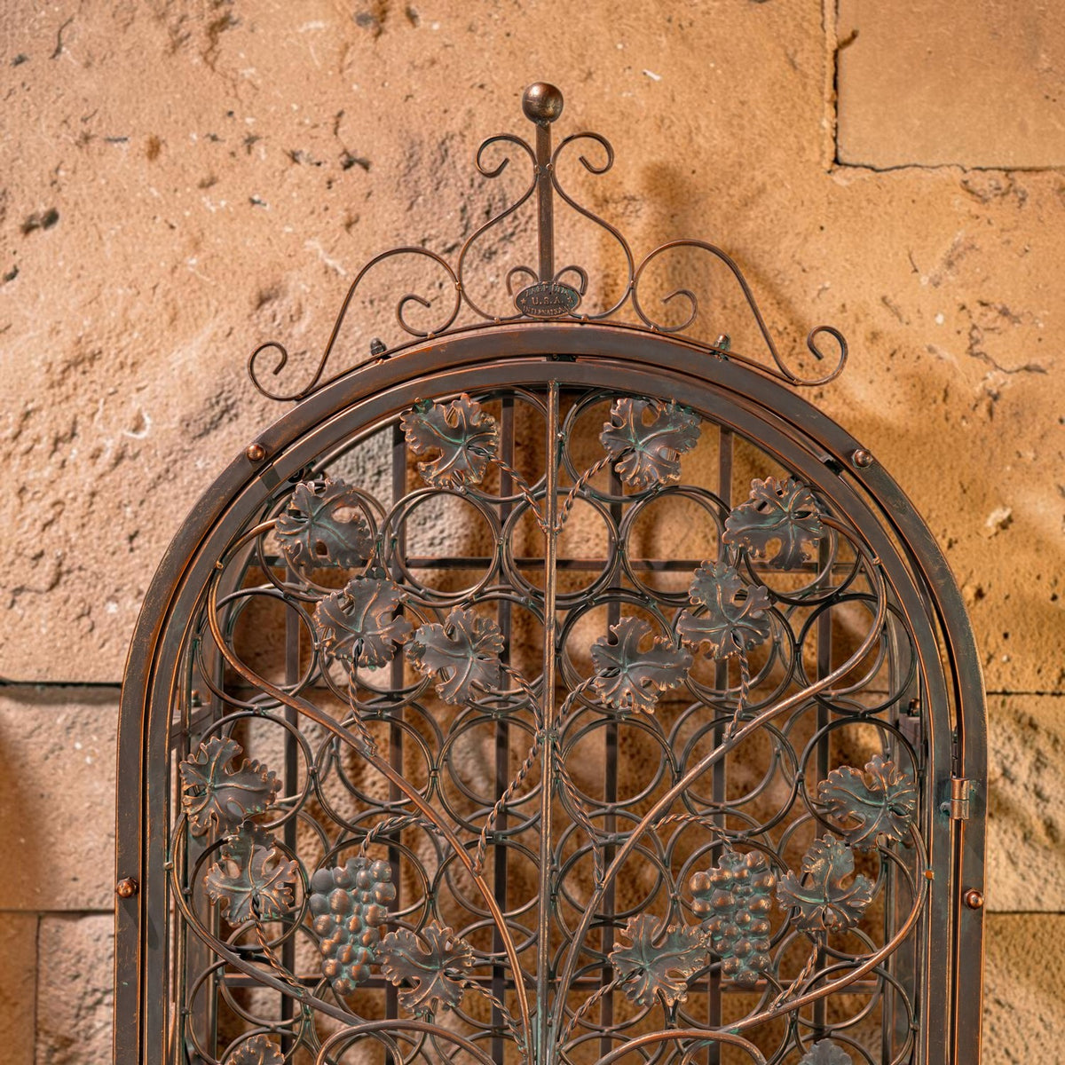 Close-up of the cabinet’s arched ironwork, curled crest, and grapevine decorations.