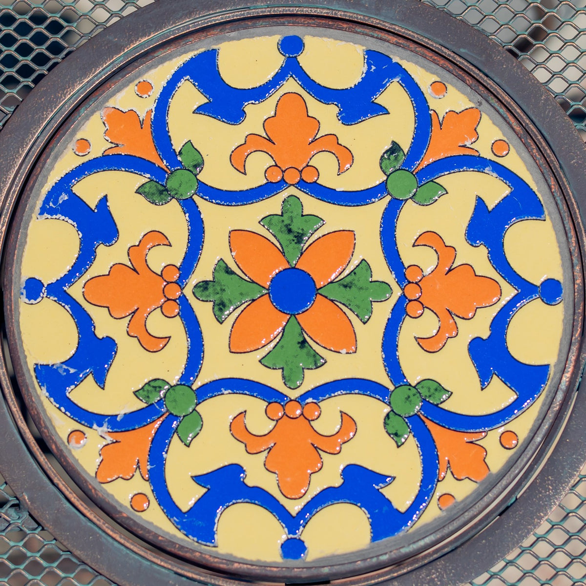 Close-up of a circular tabletop mosaic with blue, yellow, orange, and green floral motifs.