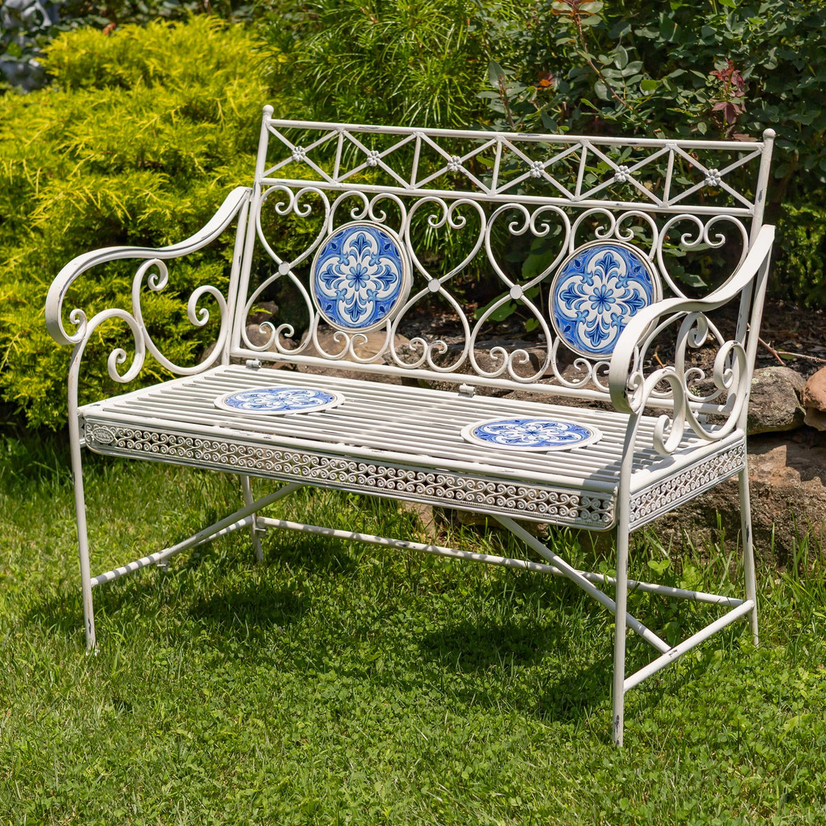 Garden bench viewed from the front, showing its decorative back, curved arms, and two blue seat mosaics.
