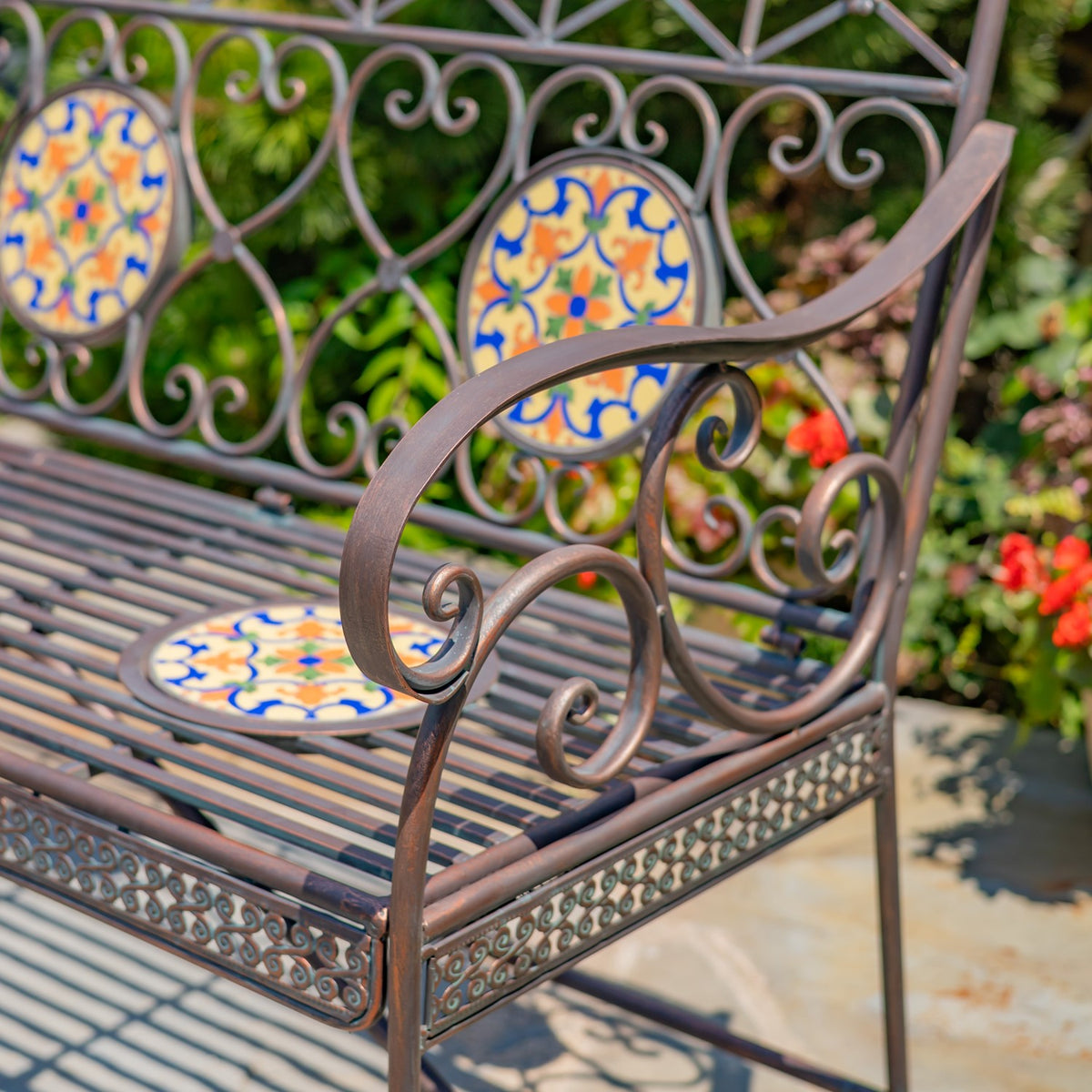 Close view of a curved metal armrest and scrollwork beside the slatted seat and mosaic back inset.