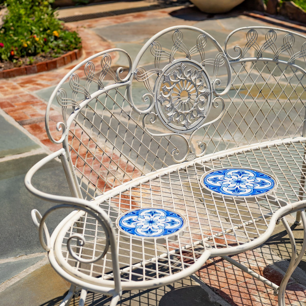 Close view of the bench’s scrollwork backrest and blue-and-white mosaic seat insets.