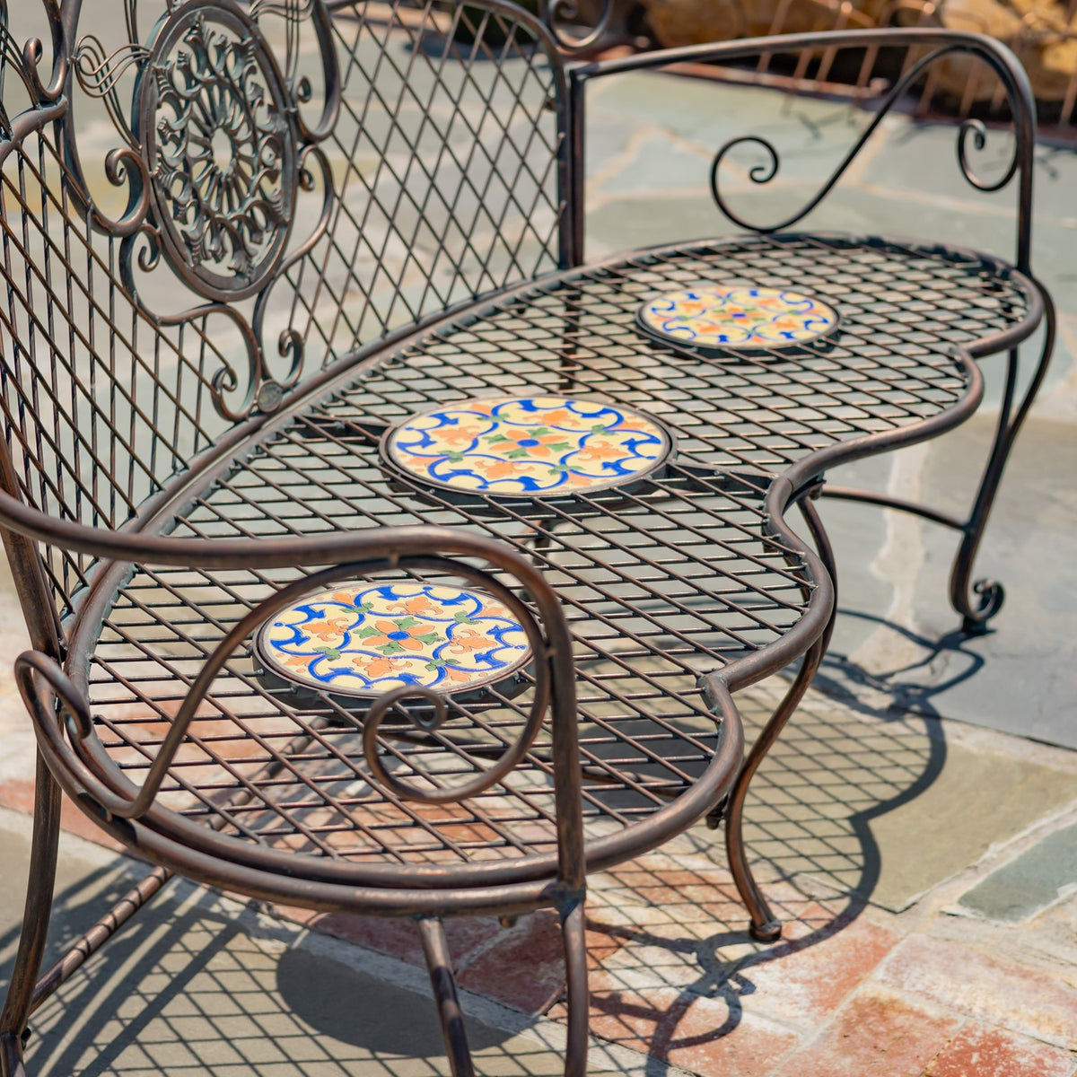 Close view of the mesh seat and three patterned mosaic tiles framed by curved metal arms.