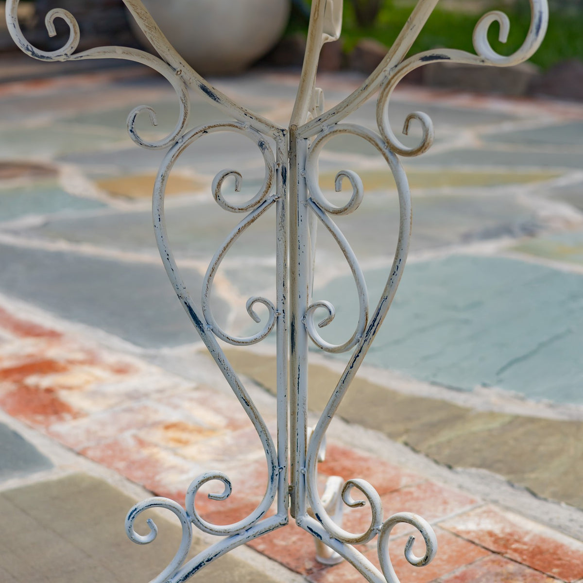 Close-up of the stand’s pale metal center support with curved scrollwork and distressed finish.
