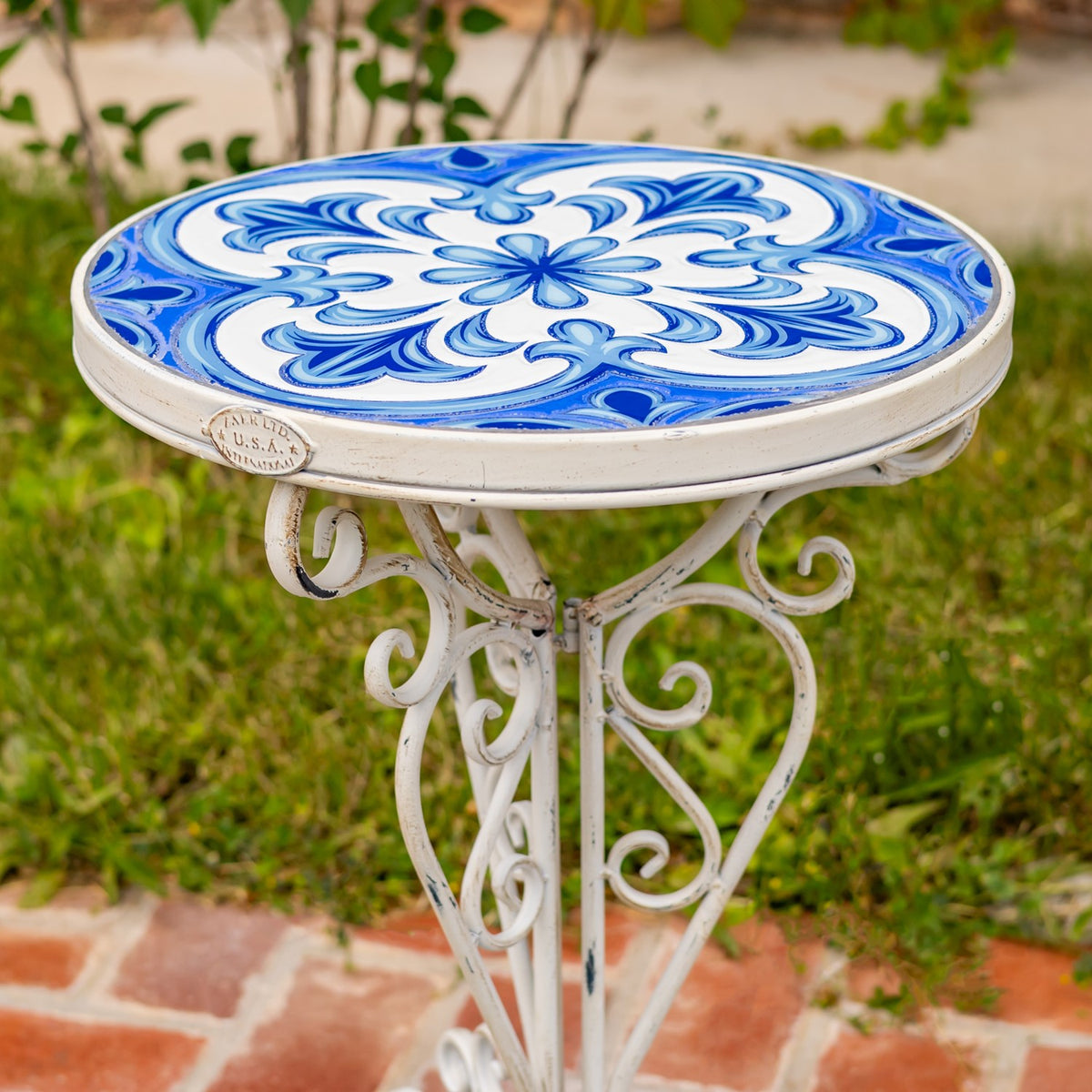 Close view of the blue floral mosaic tabletop and ornate white metal scrollwork beneath it.