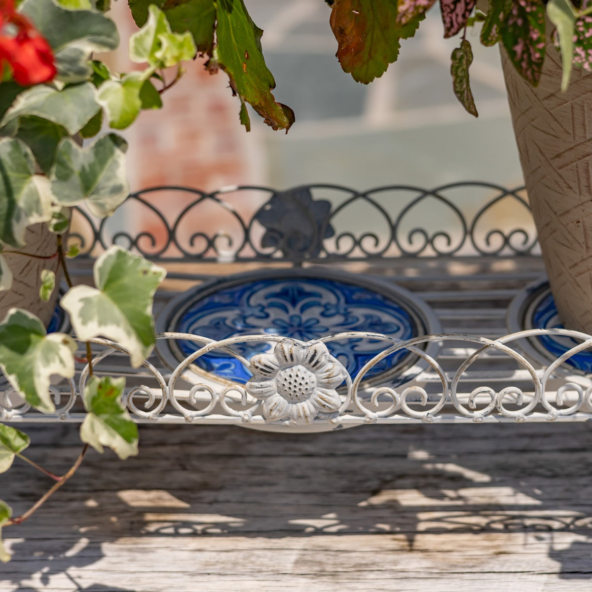Close-up of a blue mosaic panel and flower-shaped ornament on the stand’s curled metal rim.