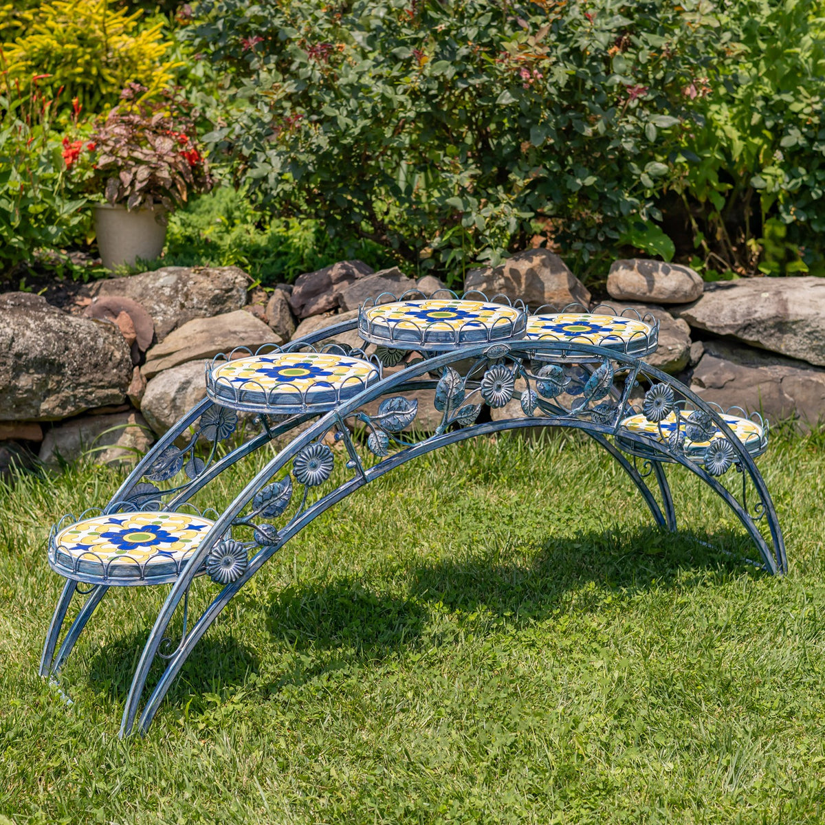 Angled view of an empty iron plant stand with floral mosaic platforms and decorative metalwork.