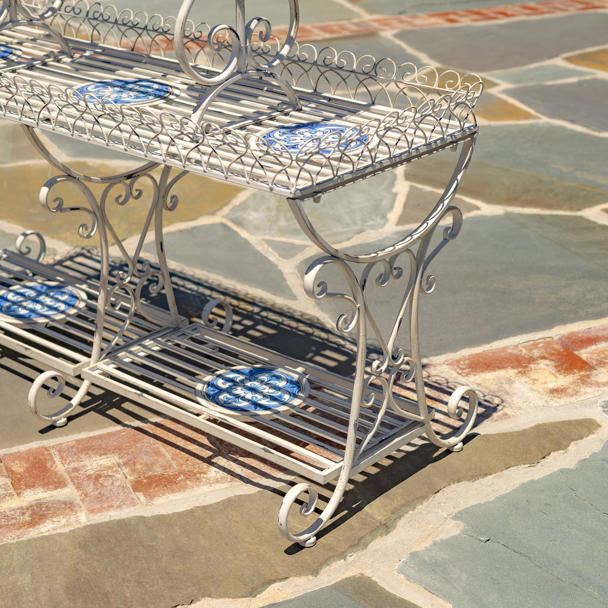 Close view of the stand’s curled iron legs, slatted shelves and blue-and-white mosaic insets.