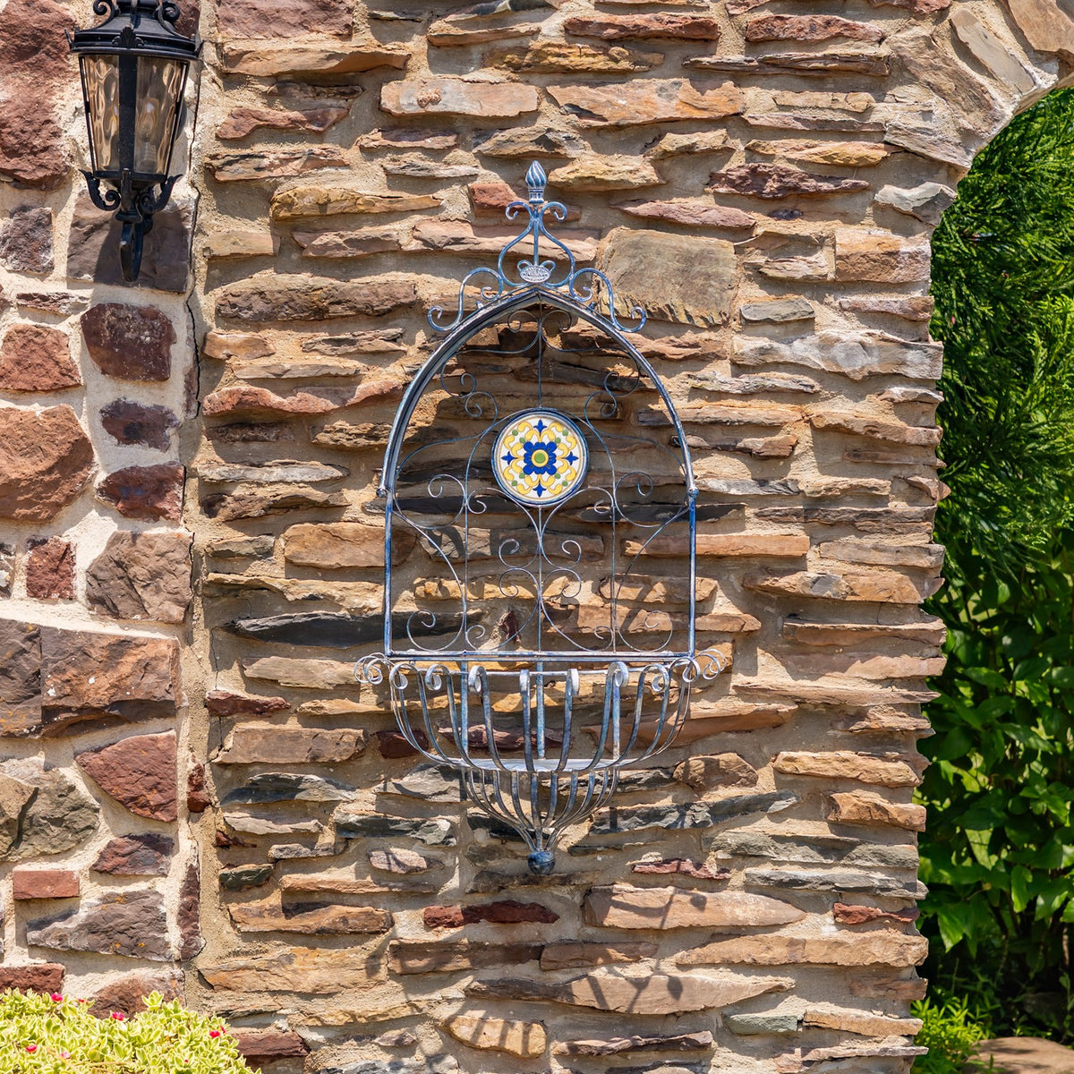 Empty blue iron wall planter with an arched frame and mosaic medallion mounted on stone.