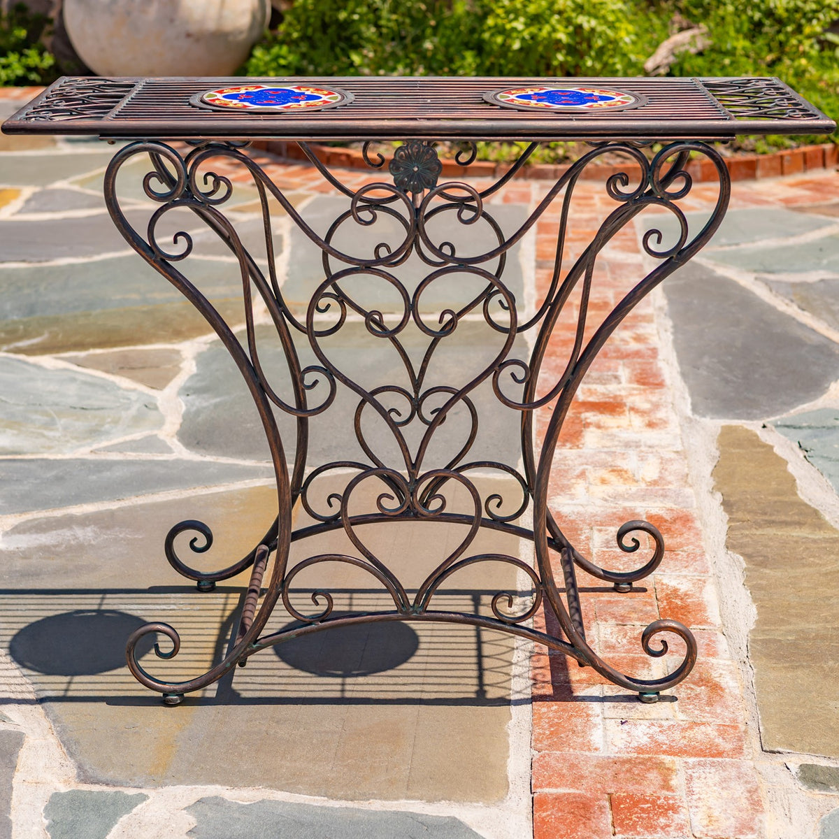 Straight-on view of the iron table, showing its symmetrical scrollwork base and two colorful mosaic circles.
