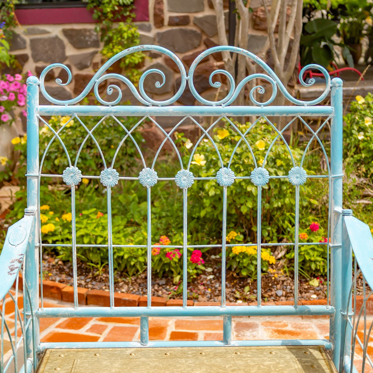 Close view of the turquoise chair’s ornate scrollwork back, with the seat edge and garden behind it.