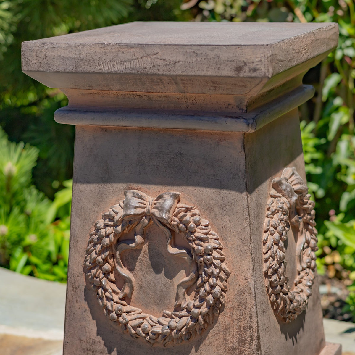 Close-up of a square column top and raised wreath-and-bow decorations on its sides.